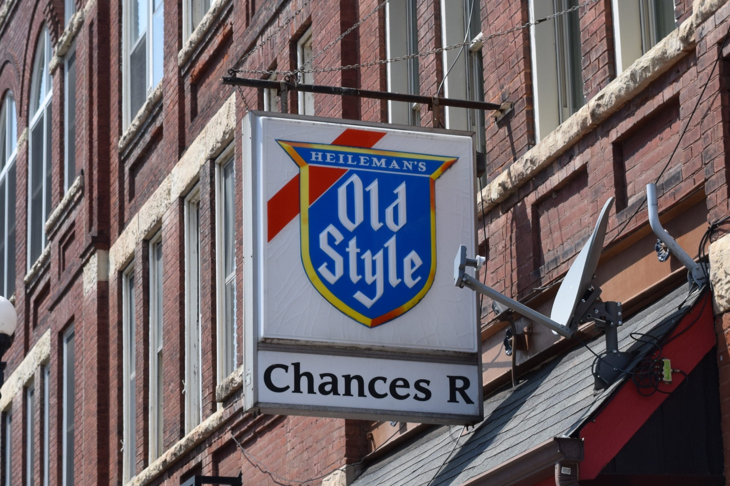 A white sign with the blue Old Style logo hangs from a brick building