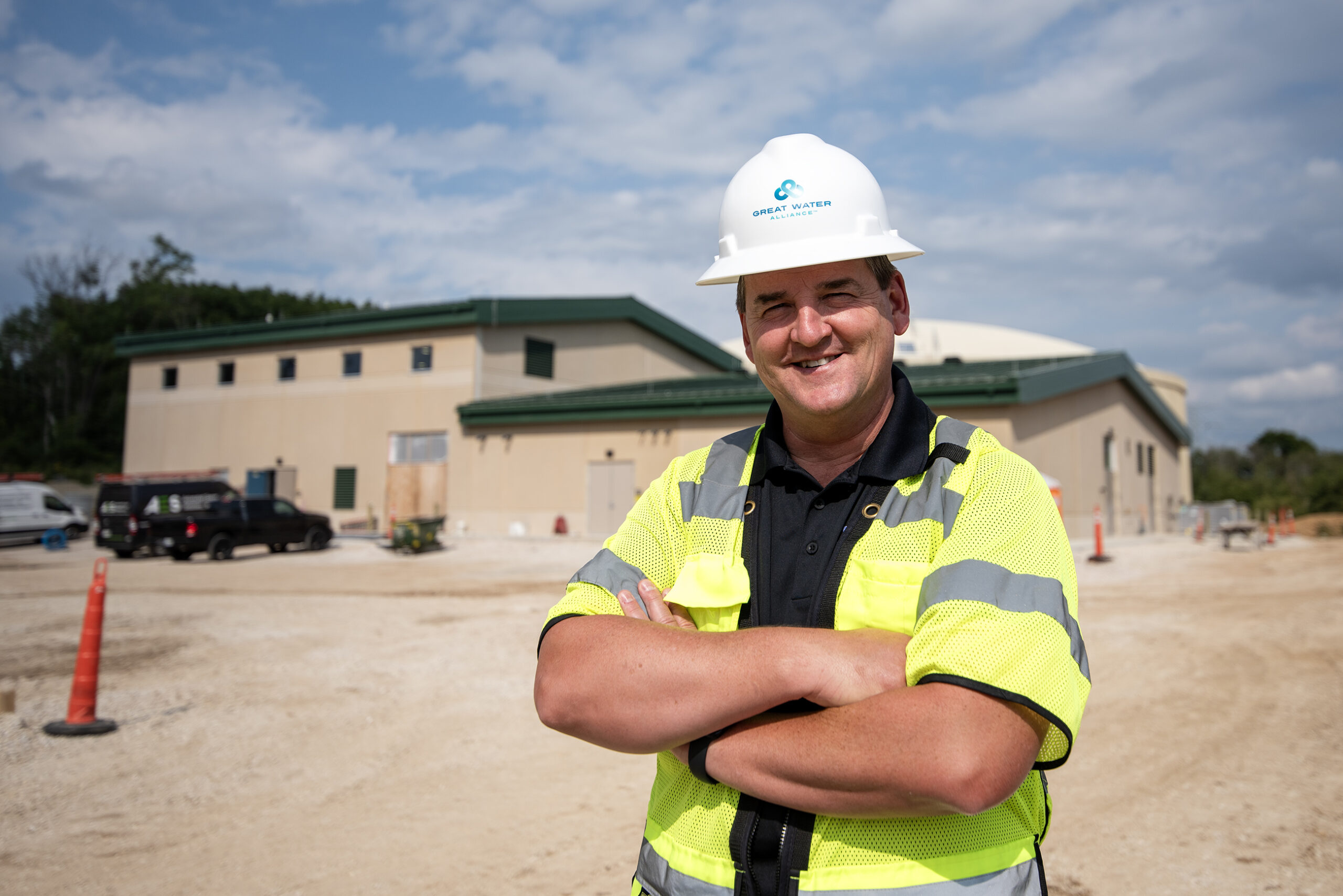 A man in a hard hat and neon vest outside a facility building.