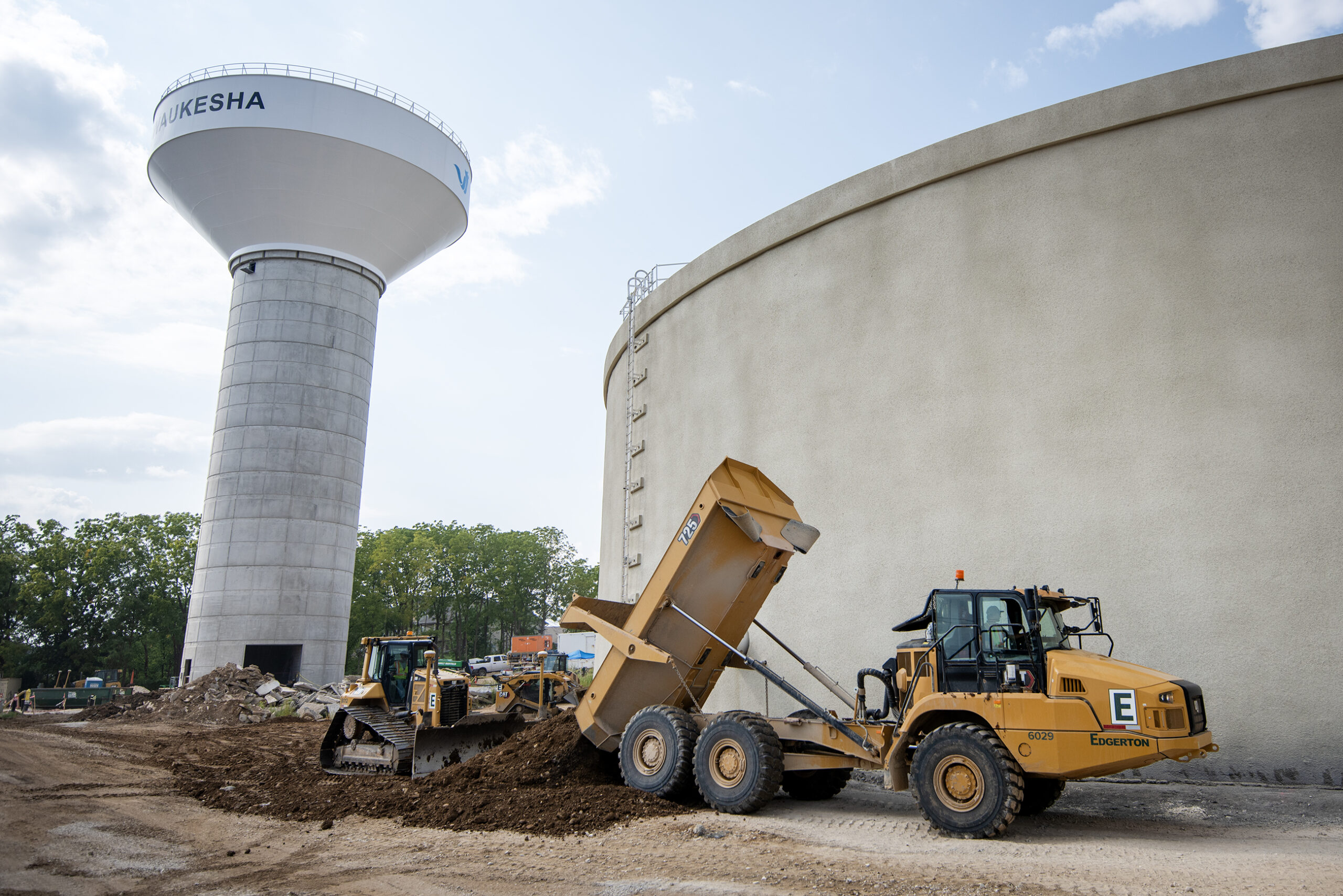 A yellow dump truck is emptied near water tanks.