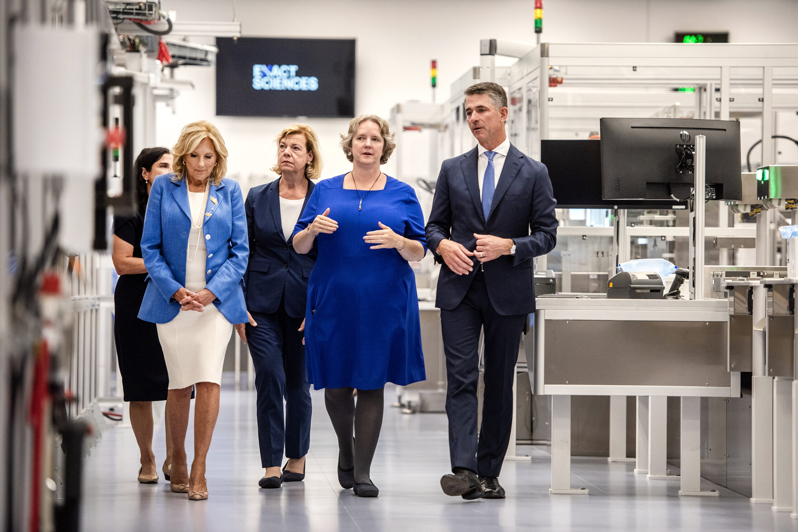 Elected officials and leaders at the lab walk in a hallway through machinery.