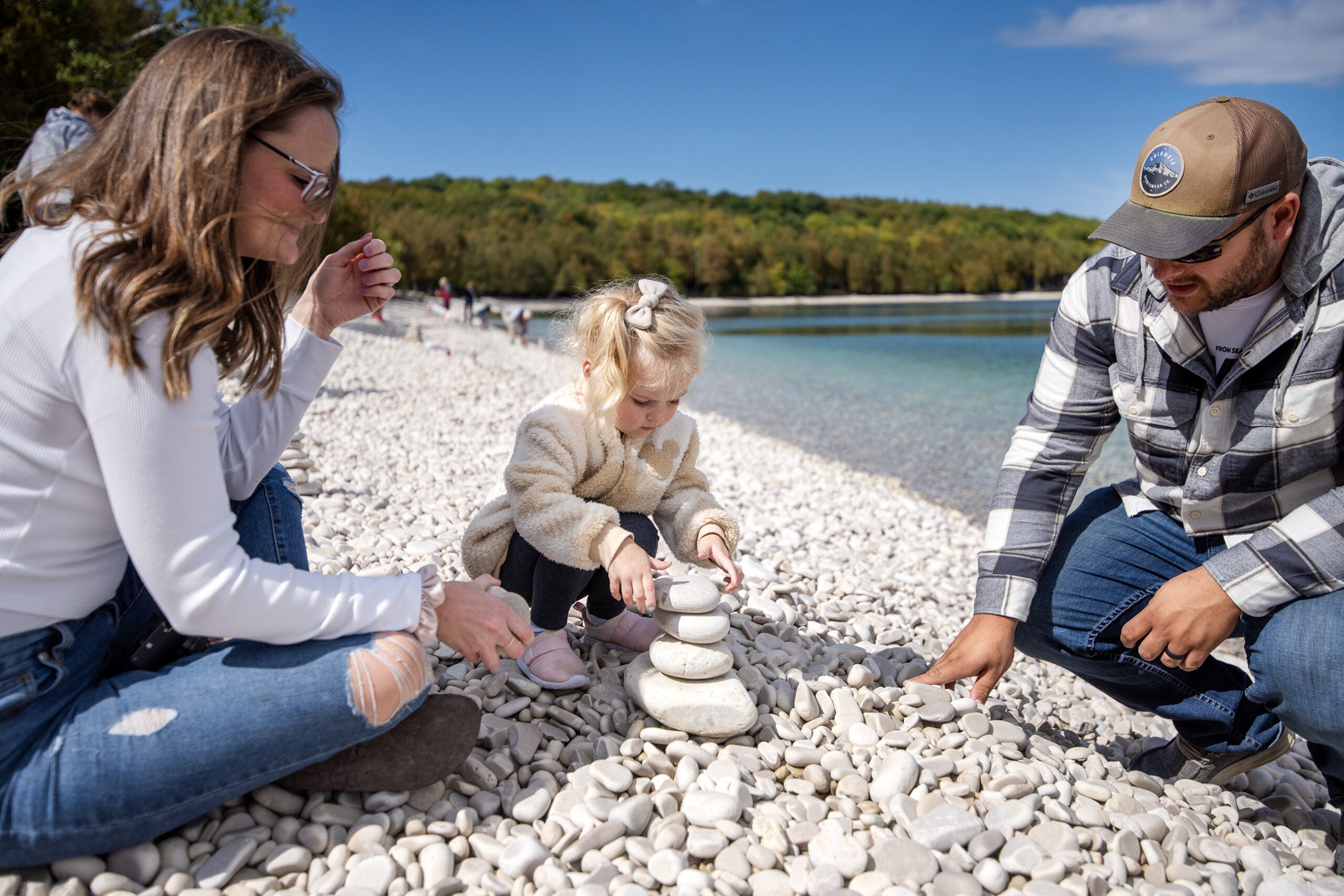 A young girl stacks light tan stones on a beach.