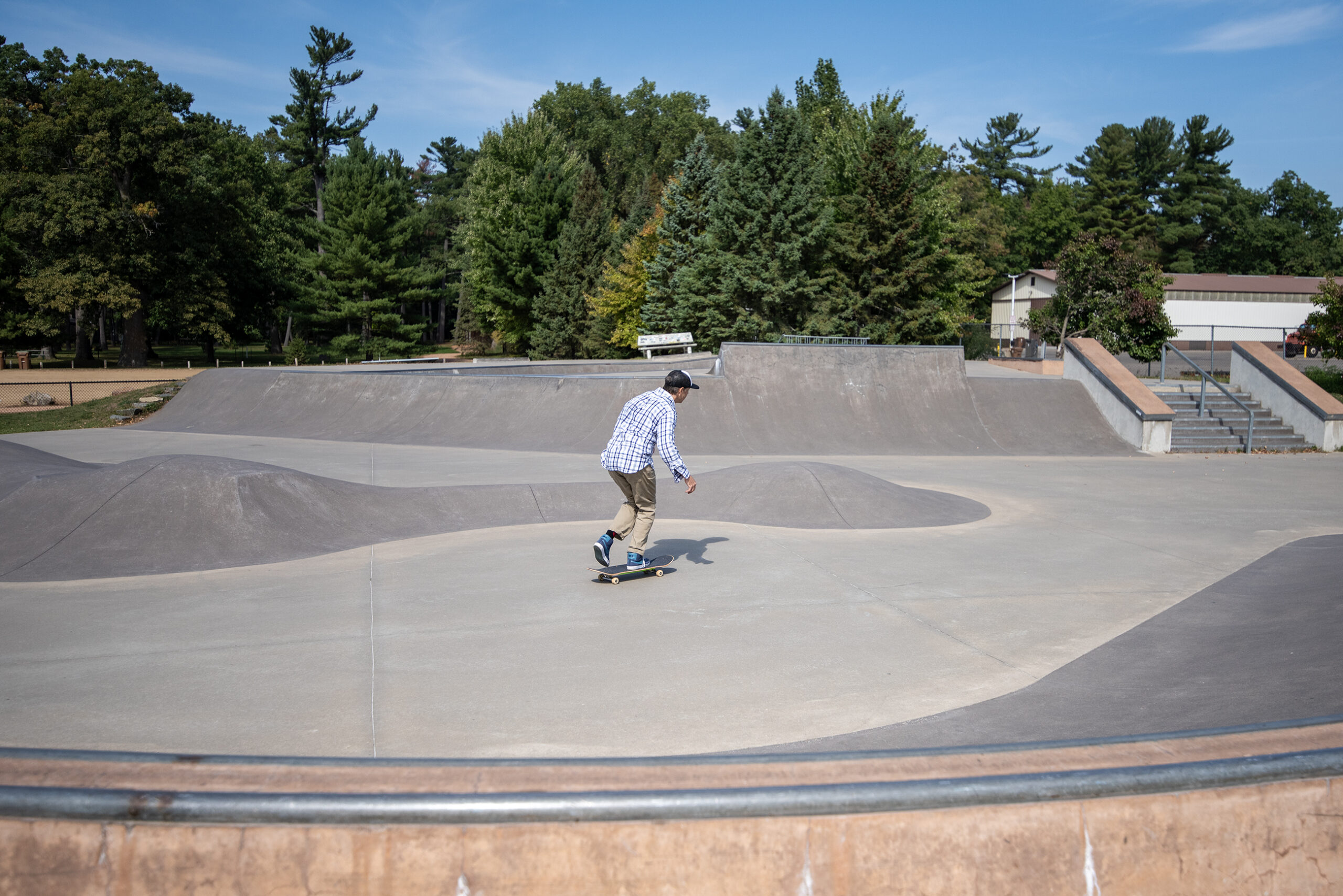 John skateboards across a concrete skate park.