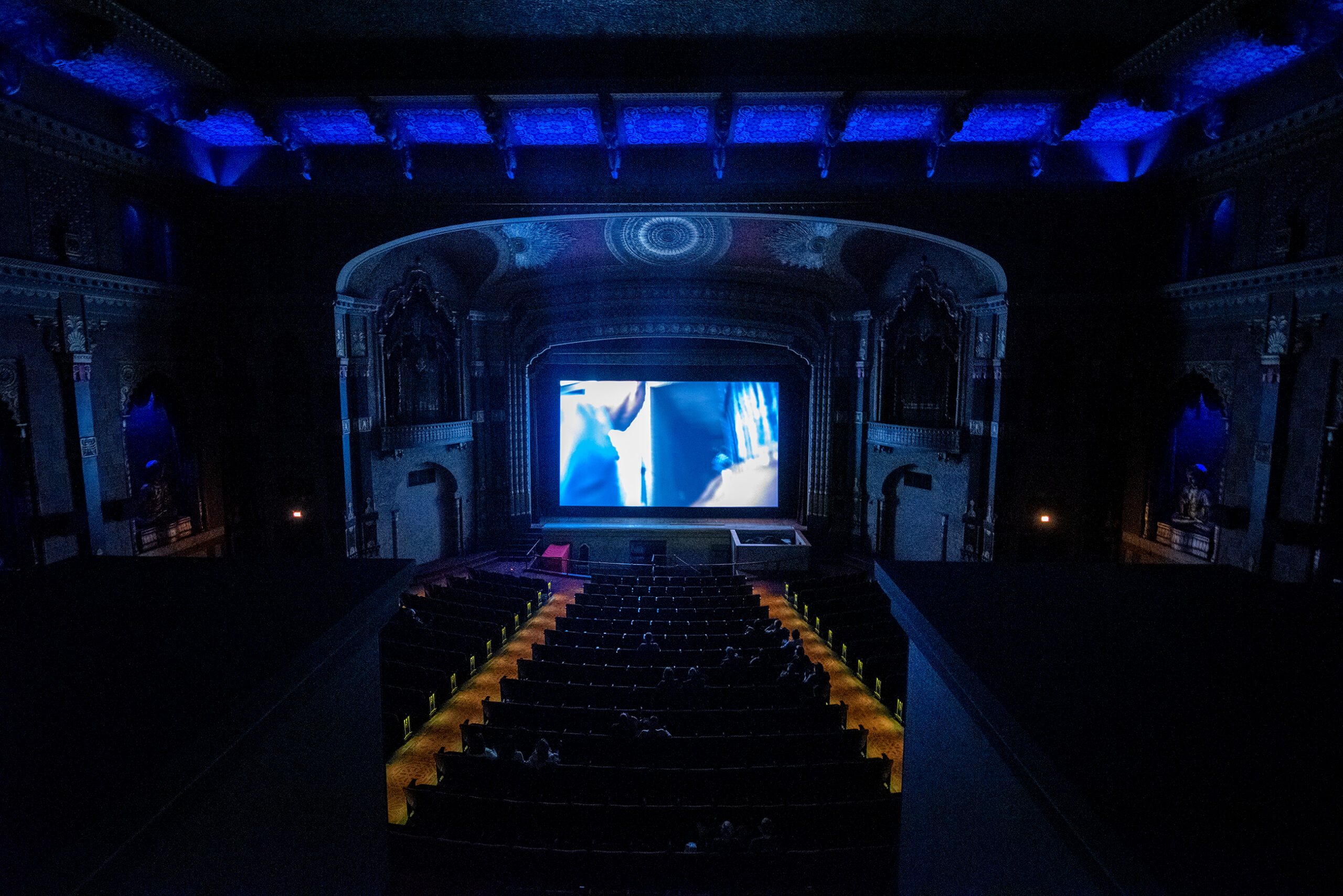 An ornate movie theater is dim as a movie is shown.