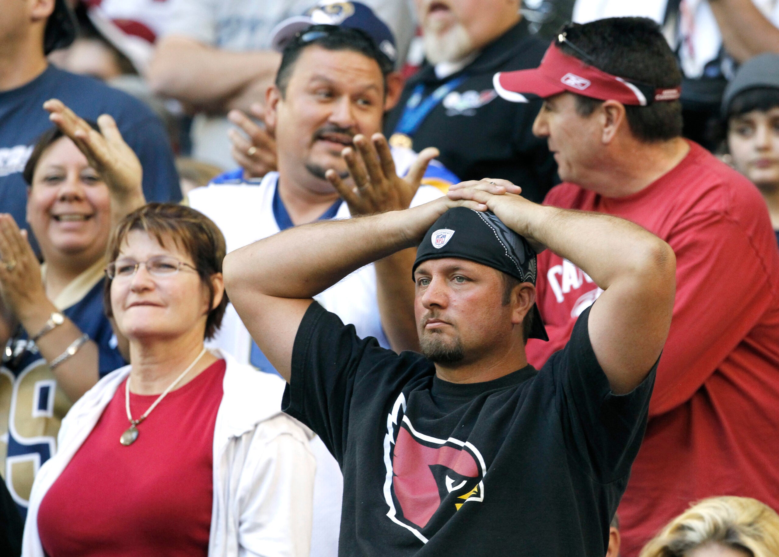 A crowd of people stand in the bleachers of a football stadium. A few look frustrated.