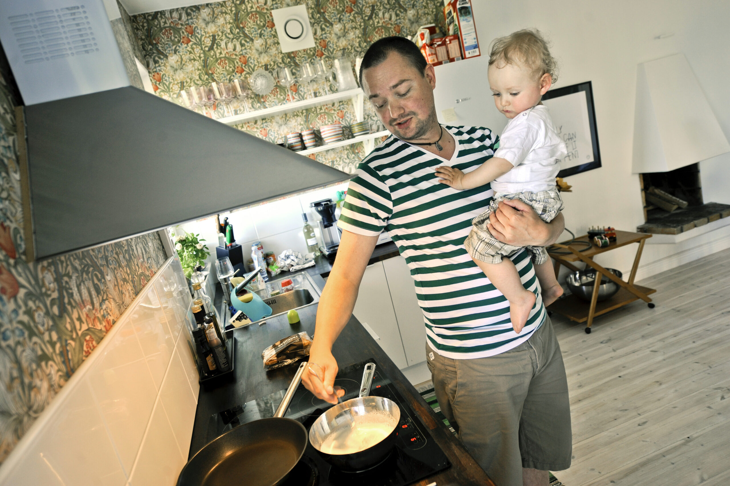 A Swedish man cooks while holding his son in his other arm