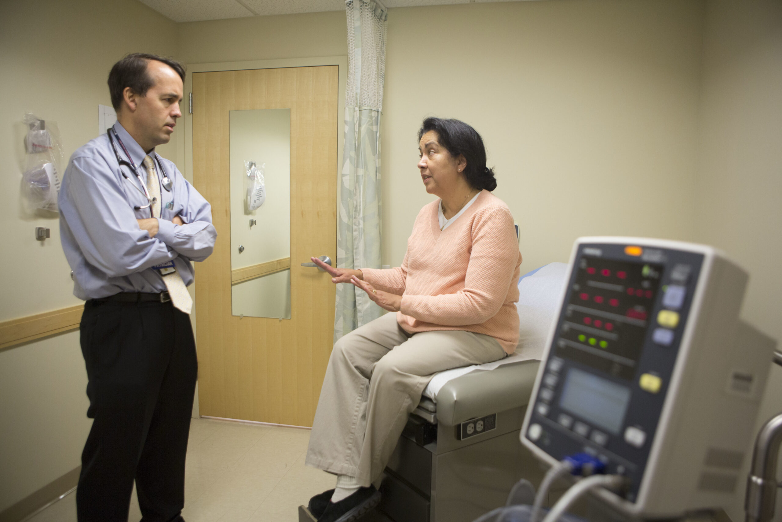 A person sitting on a medical examanation table talks with a doctor.