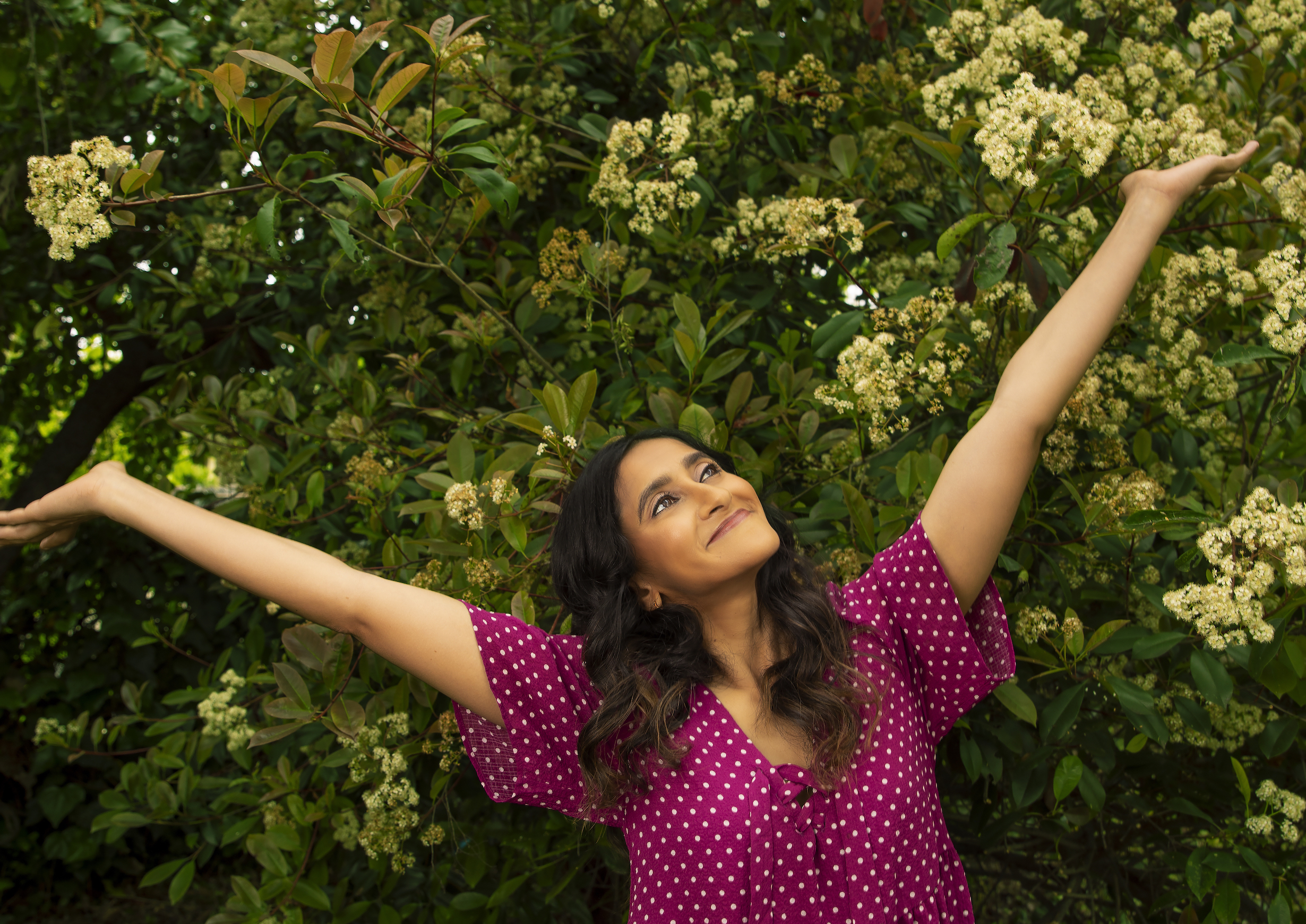 Aparna Nancherla with her arms outstretched in front of flowers