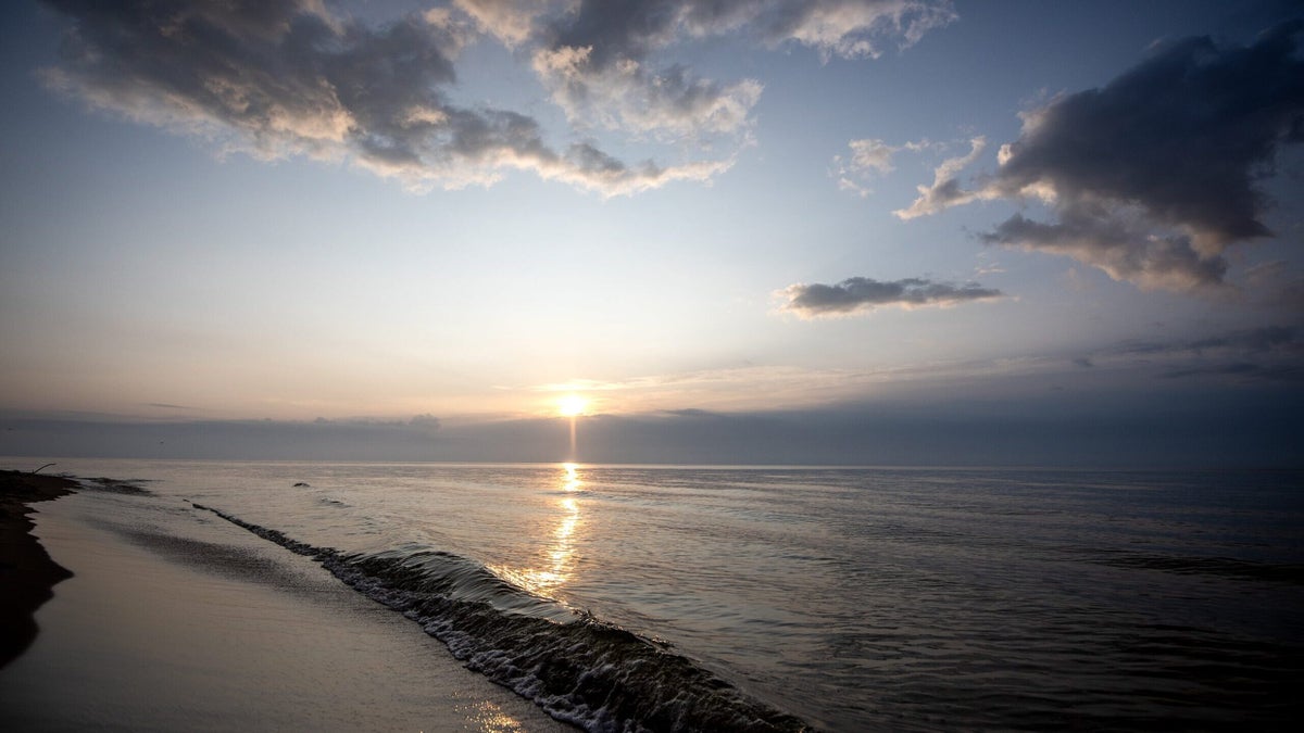 The sunrise reflects on the water as small waves lap up on the shore.