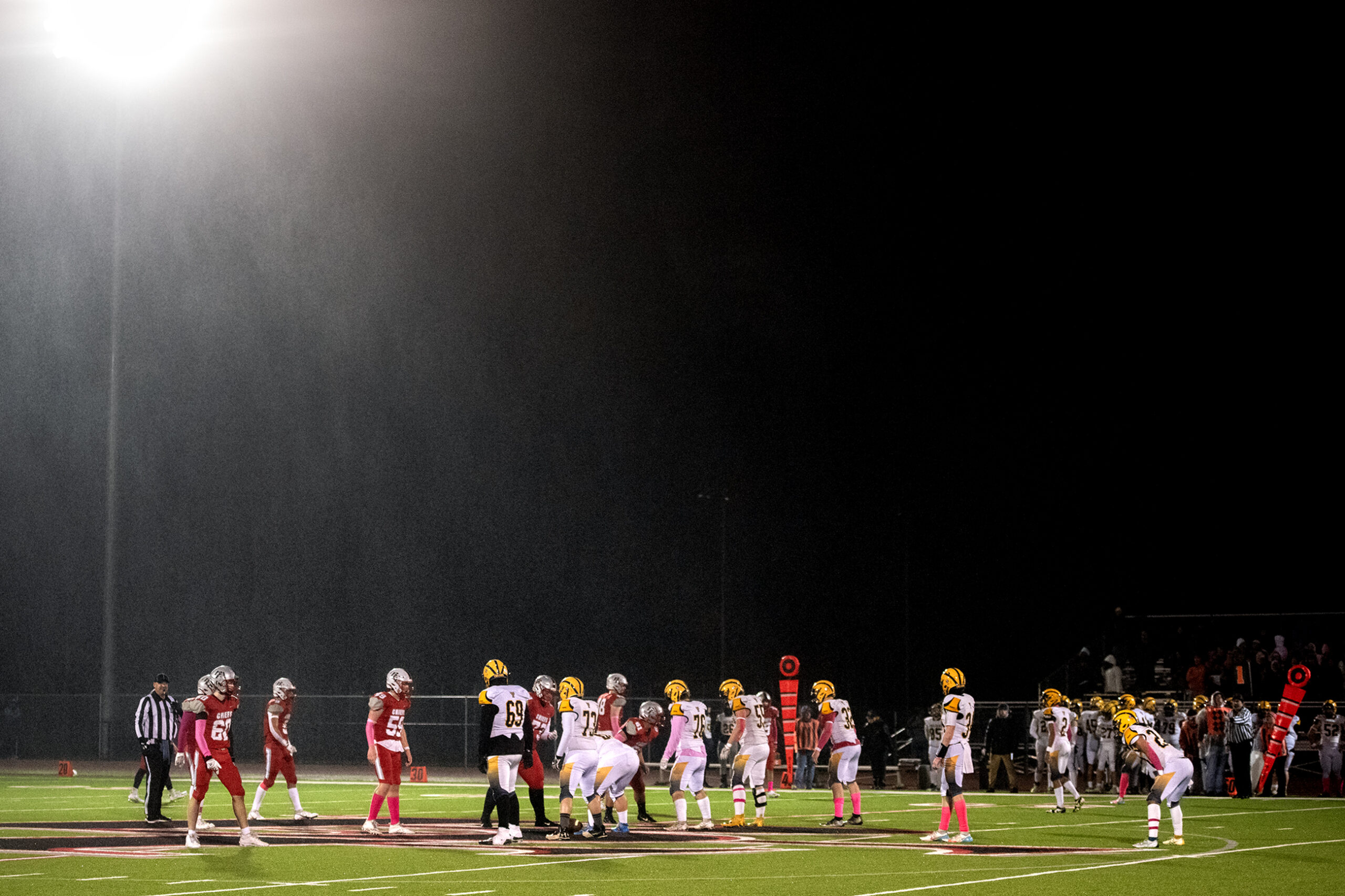 Rain is illuminated by a stadium light as a game takes place on the field below.