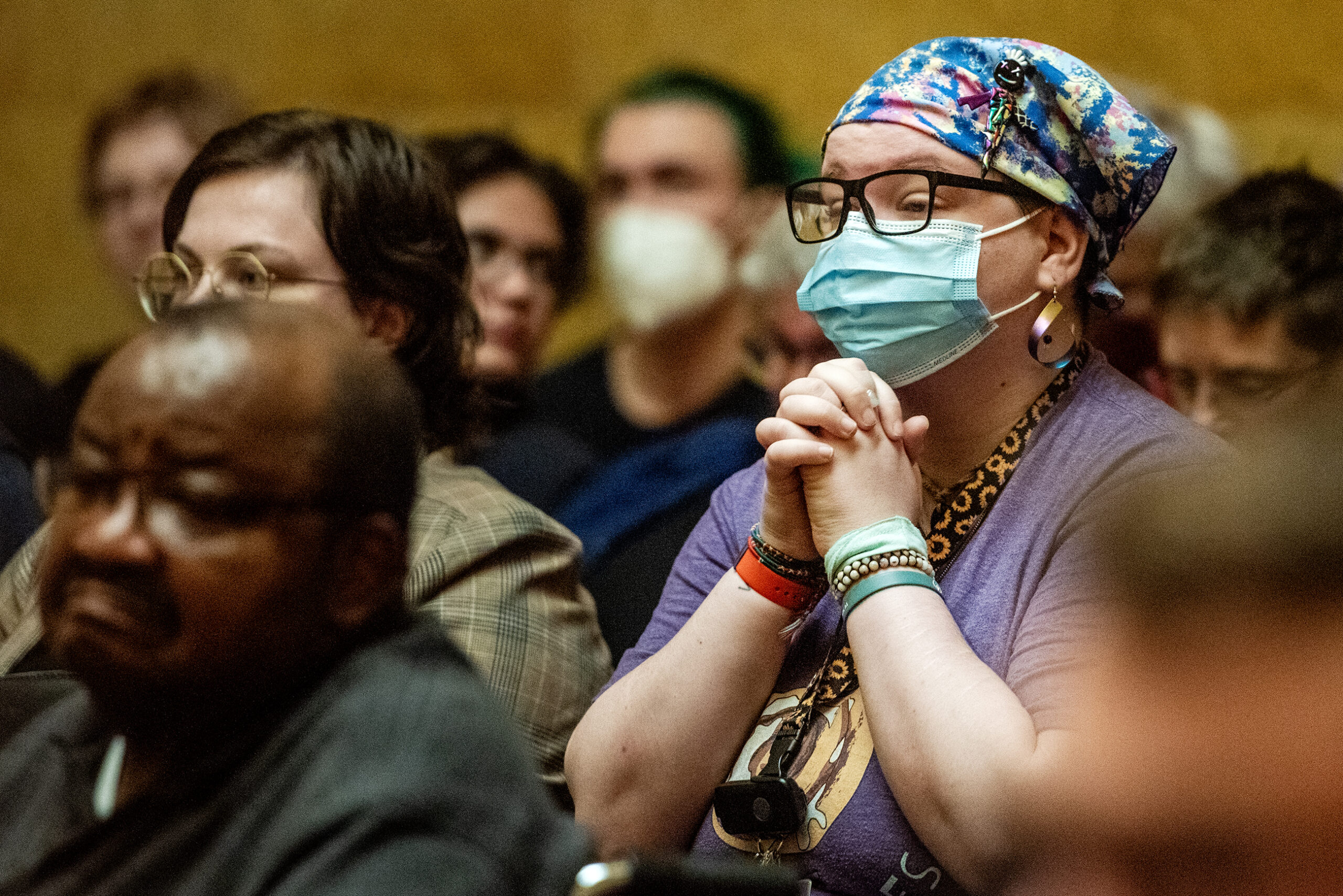 A person clasps their hands as they listen.