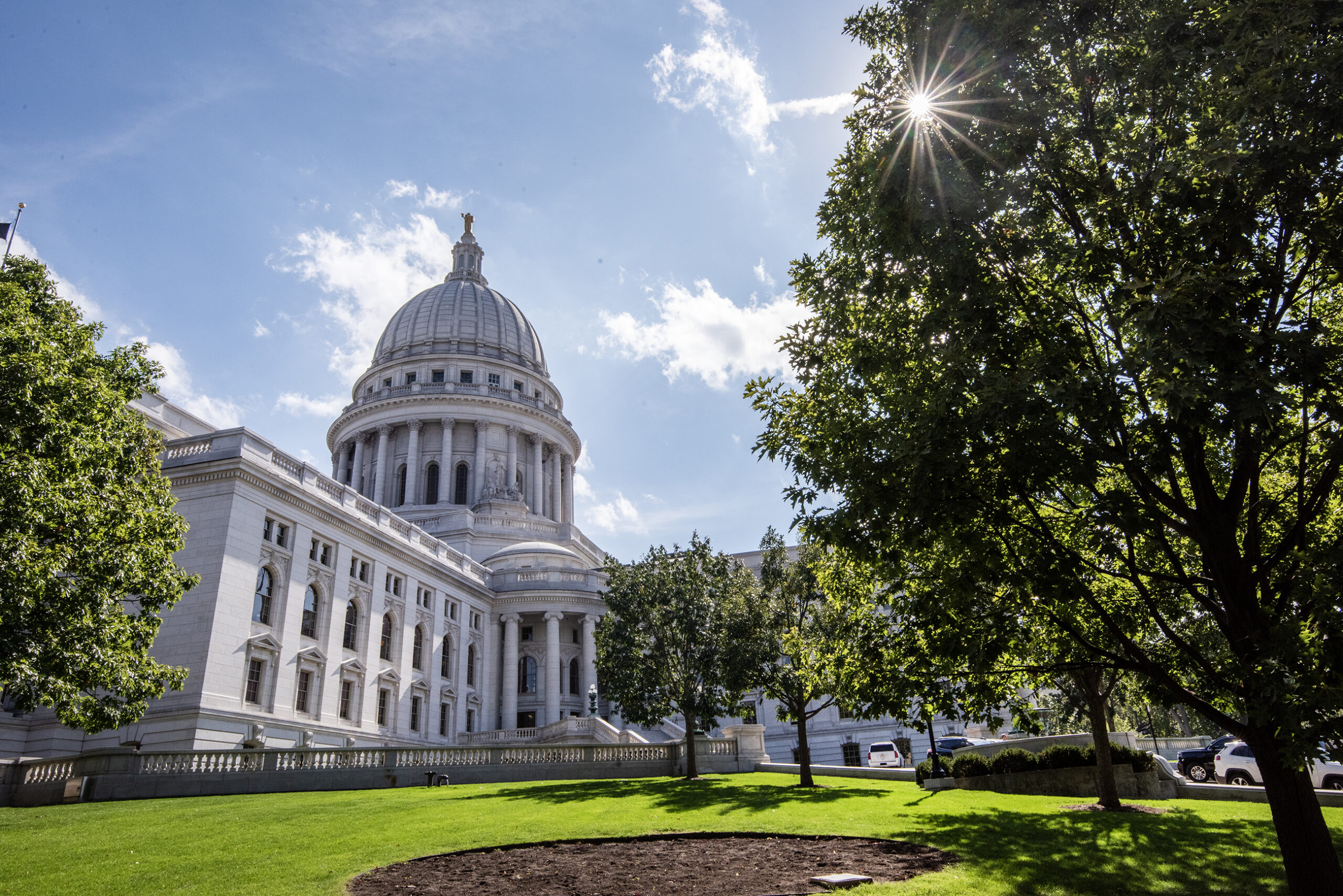 The sun shines through leaves in front of the Wisconsin State Capitol.