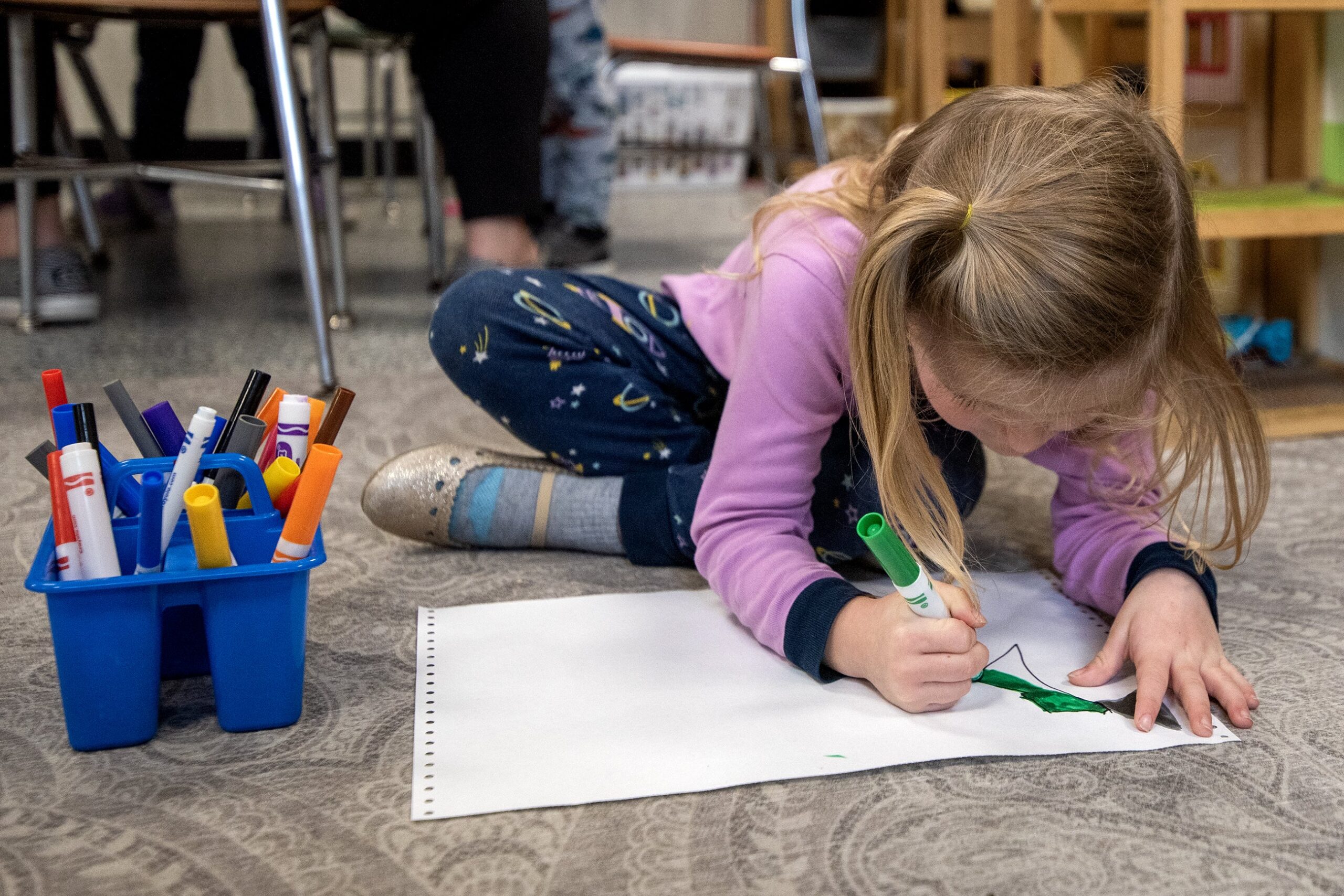 A young girl sits on the floor as she draws a picture.