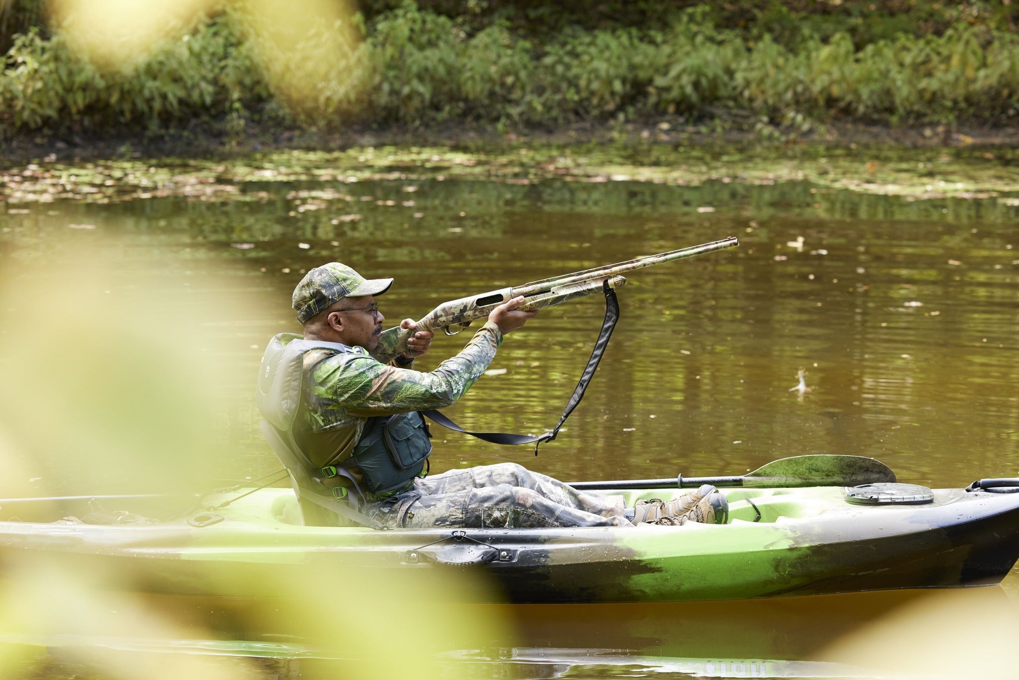 A man in a boat pointing a shotgun at the sky