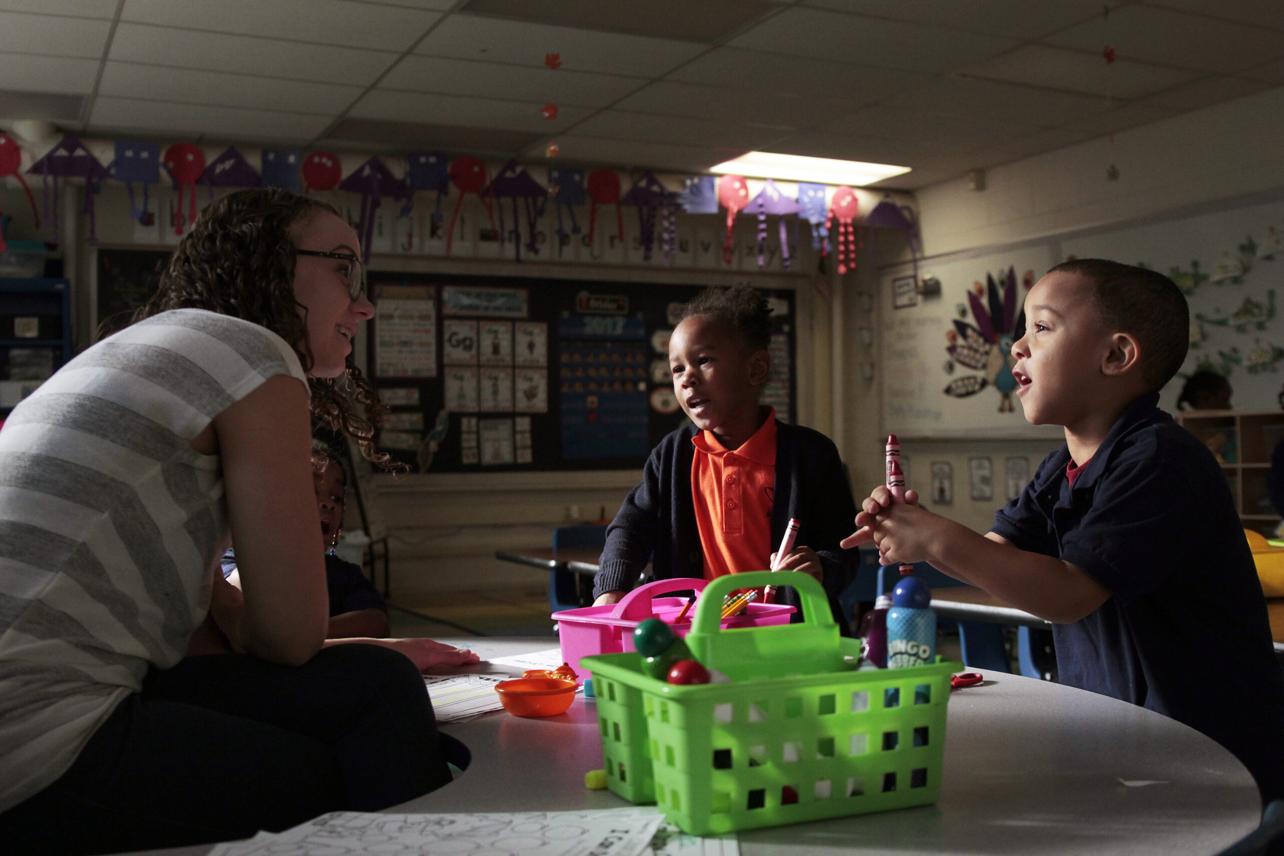 Two K-4 students speak with a teacher at a classroom table