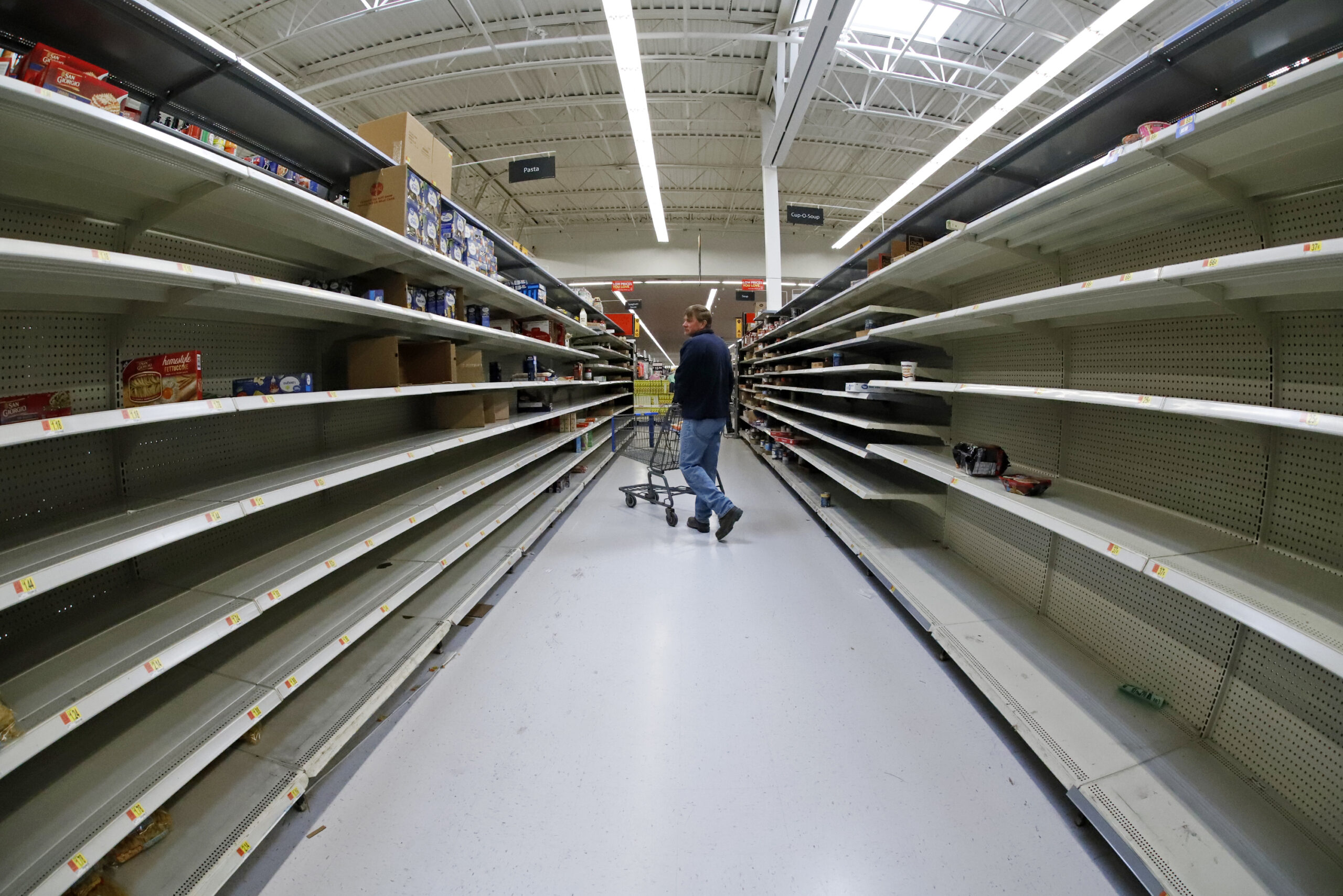 A man shops in an aisle of mostly empty shelves in a Walmart
