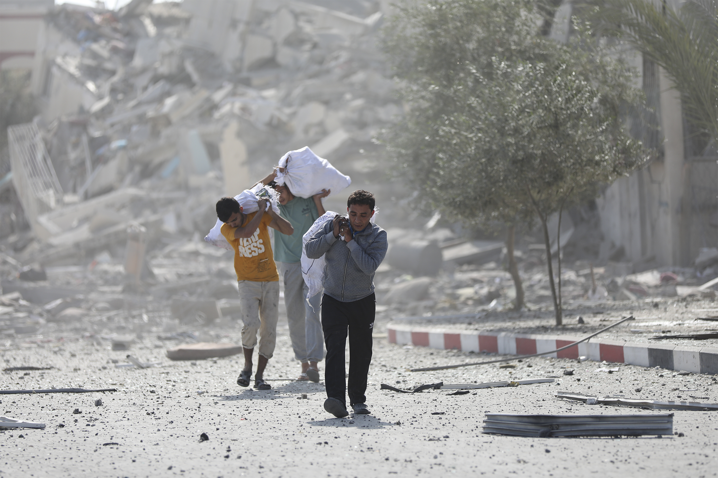 Palestinians walk carrying bags as they pass destroyed buildings