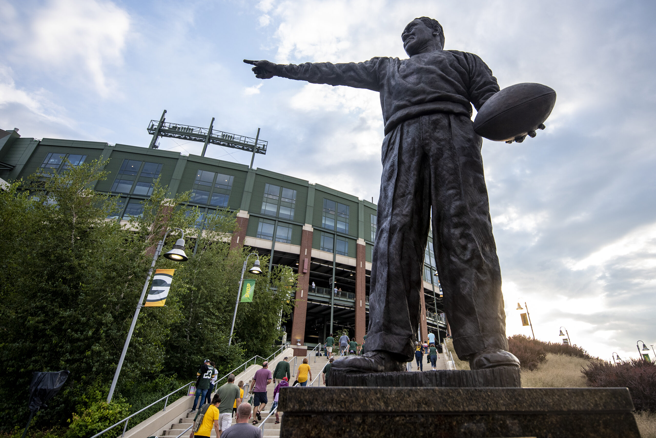 A statue of a man holding a football with his arm outstretched is seen in front of Lambeau Field.