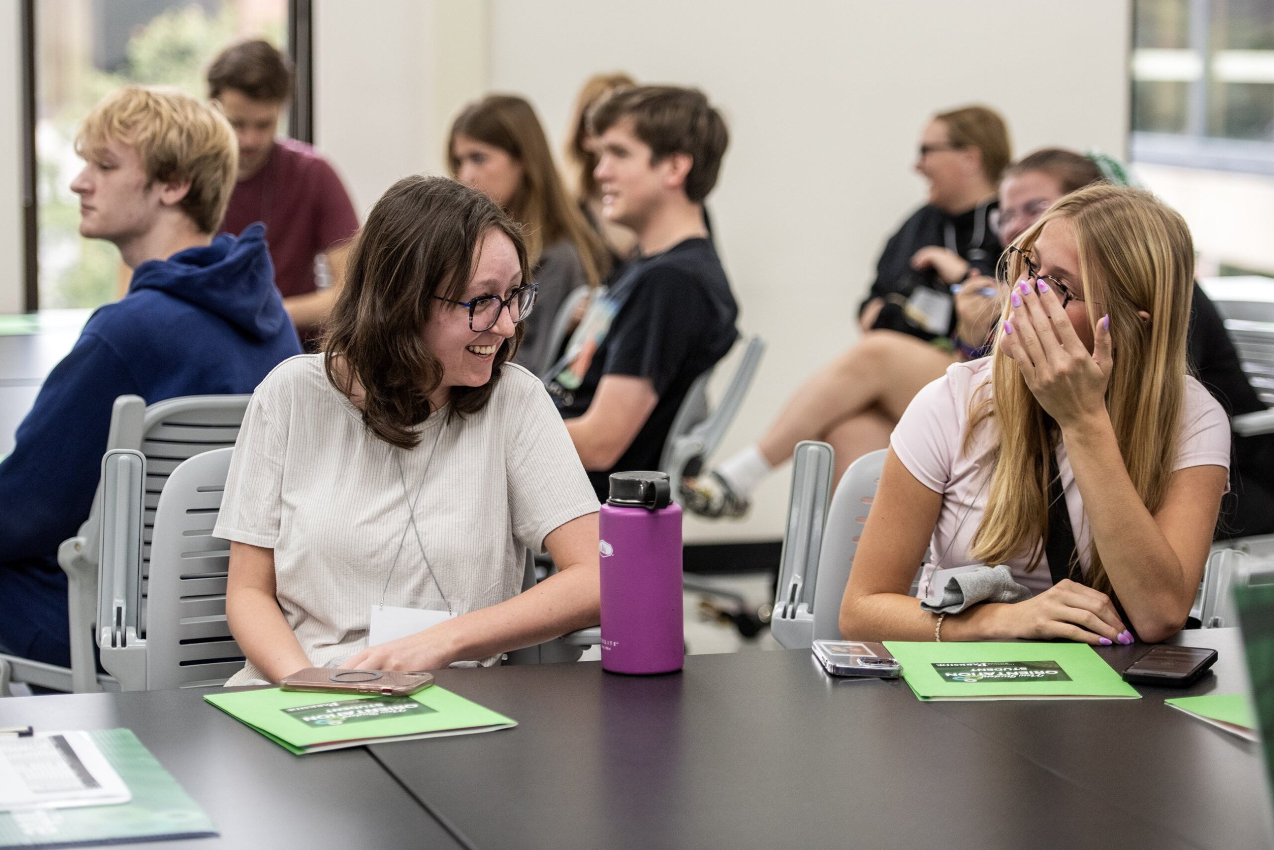 Students laugh as they play a game while sitting in a classroom.