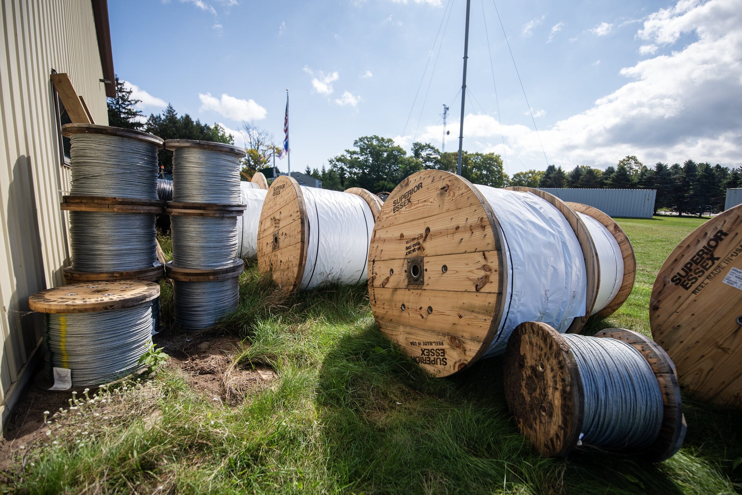 About a dozen large spools with wire sit outside on a grassy lawn.