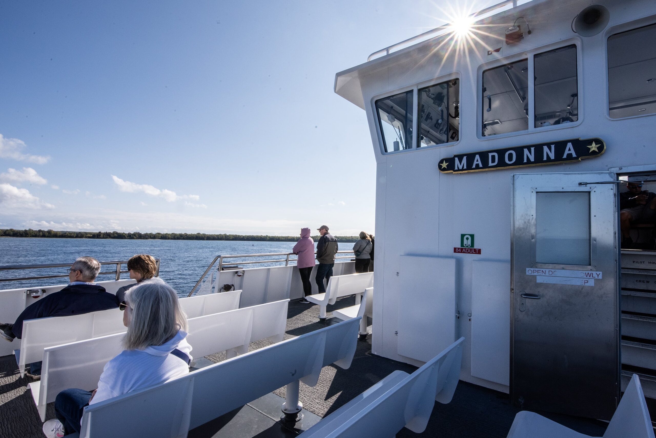 The sun peeks out from behind the ferry control room as several people sit in the outdoor seats.