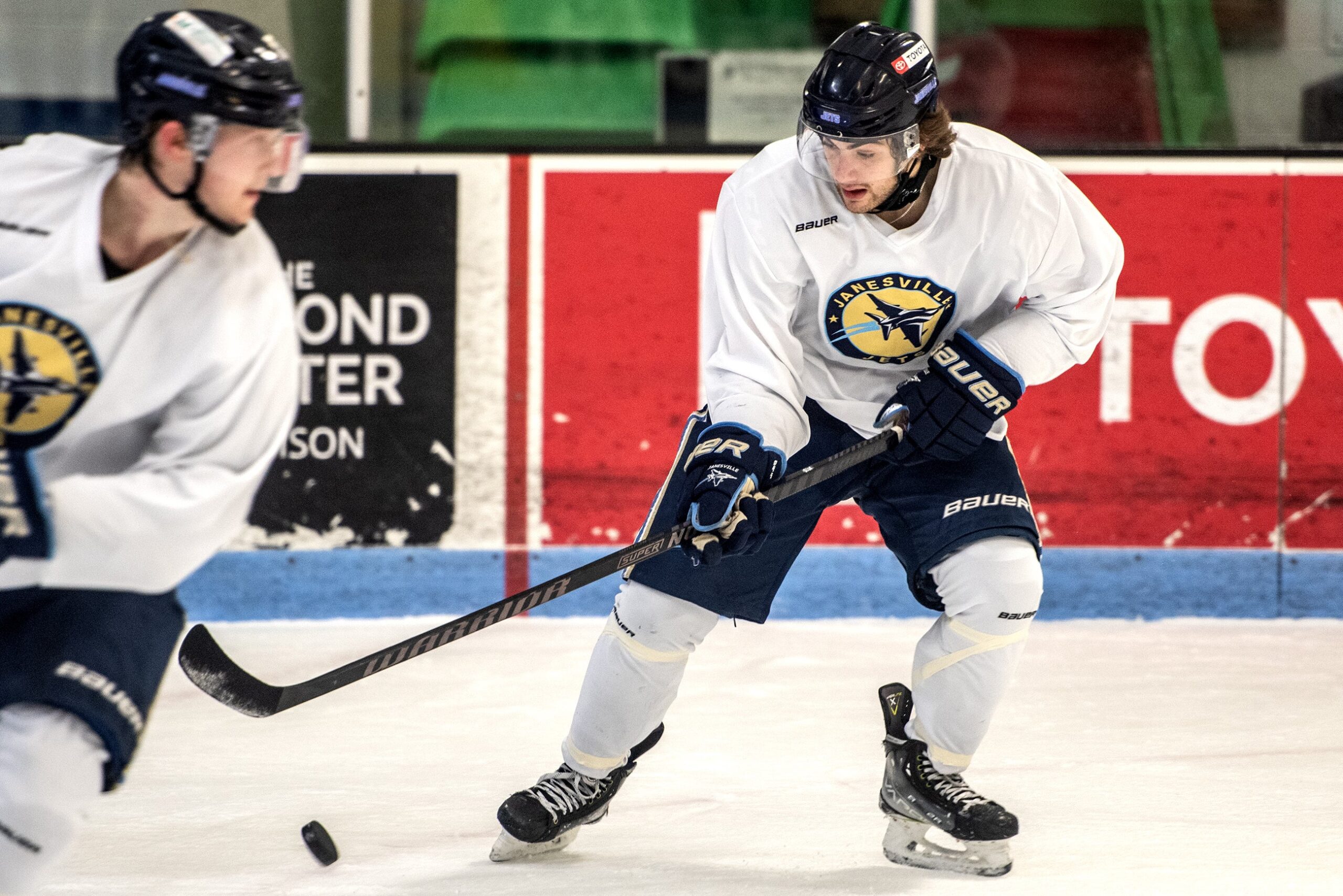 A player in a neck guard moves the puck on the ice.
