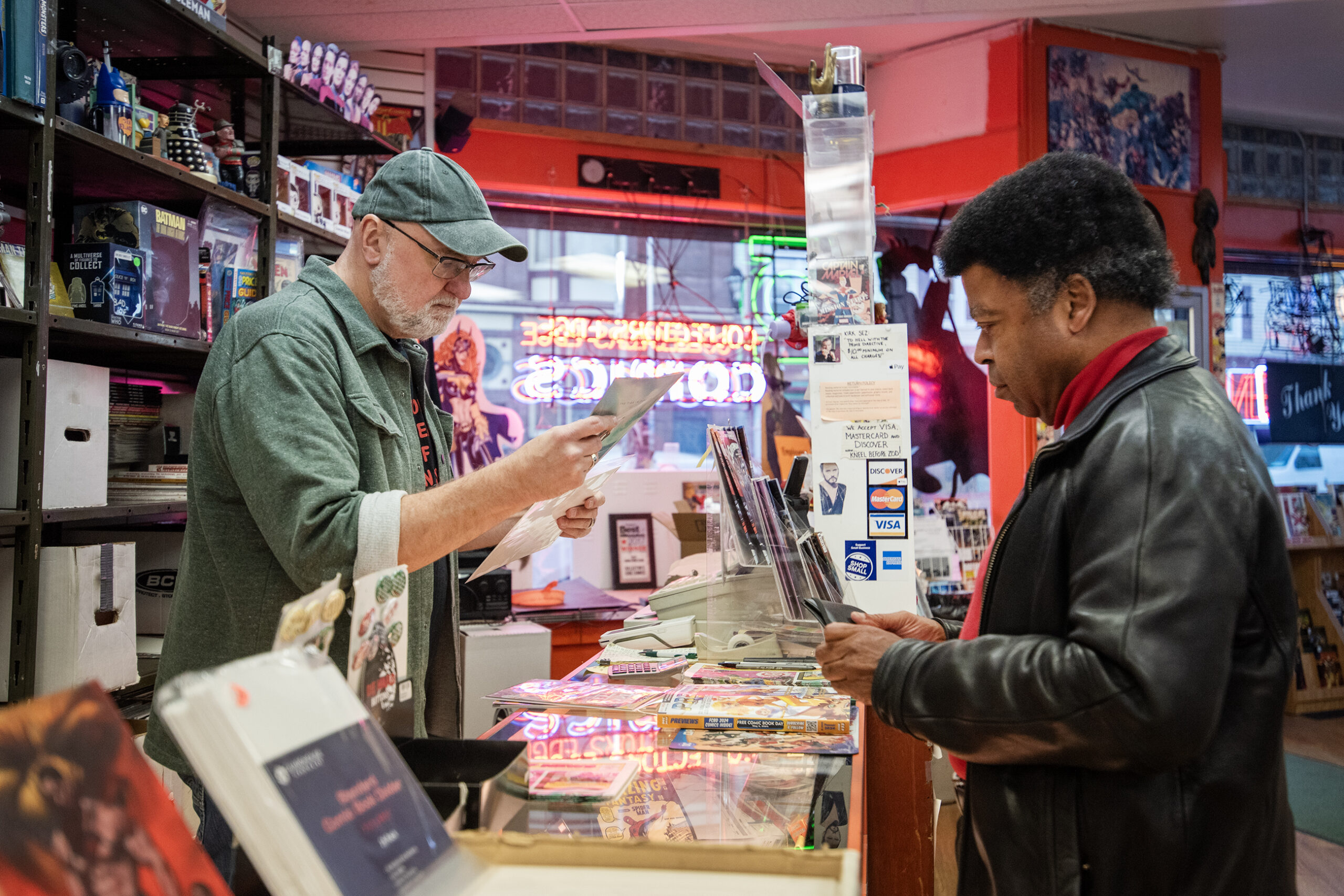 A man holds a comic book as he checks out a customer at a store.
