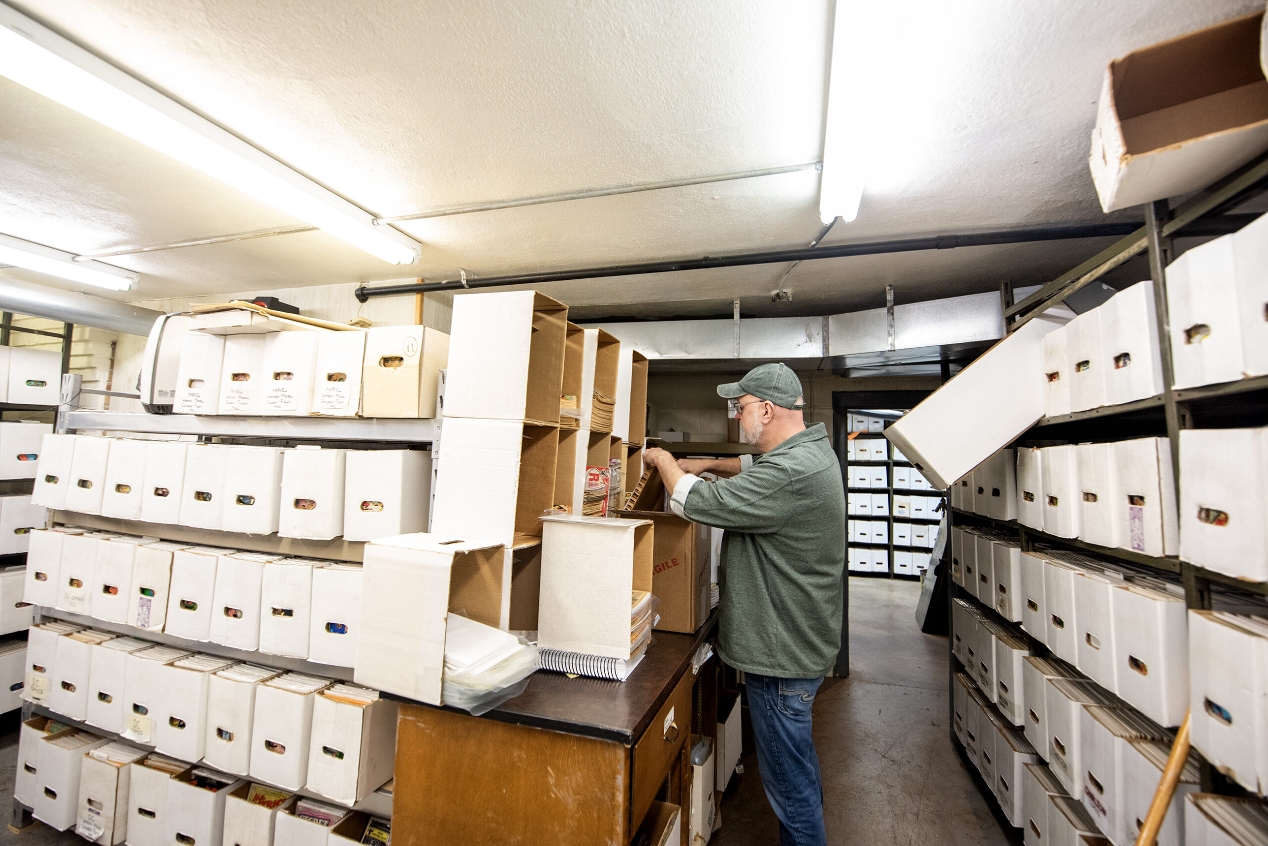 Boxes are stacked high in a storage room. A man reaches inside one of them.