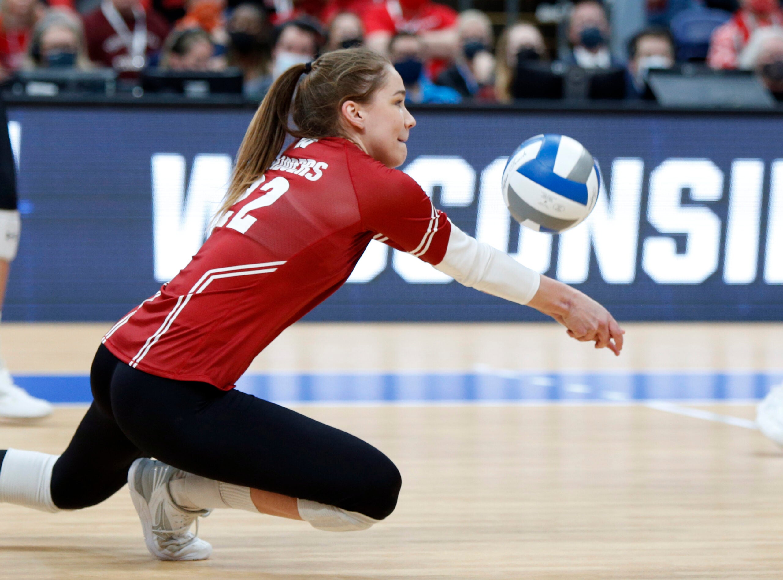 A volleyball player lunges low to the ground to dig a volleyball during a game