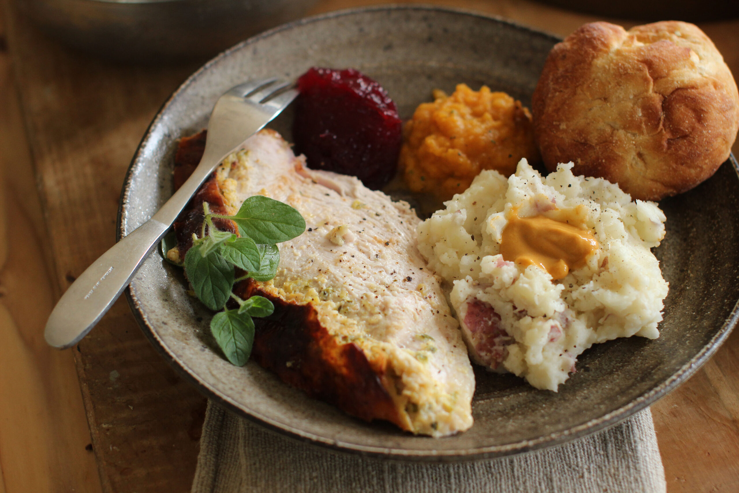 A dinner plate with turkey, cranberry sauce, mashed potato and a dinner roll.