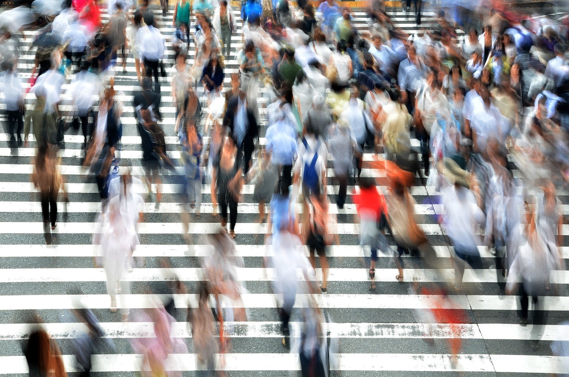 A crowd of people move over a striped crosswalk in a blur.