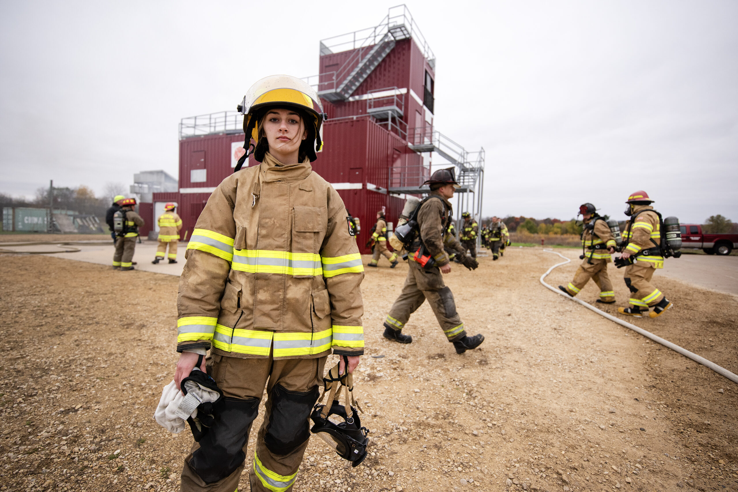 A girl in firefighting gear stands near the exercise as it goes on.