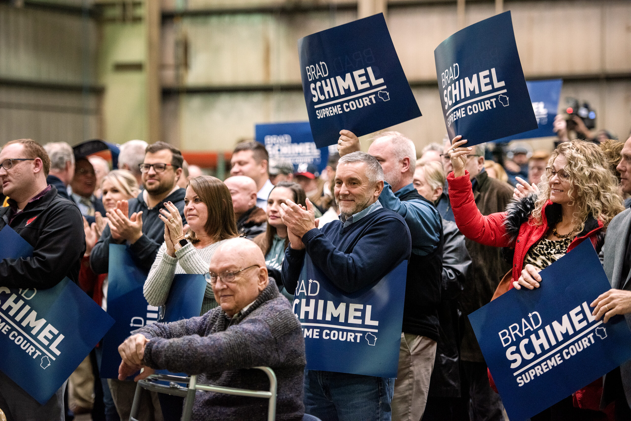 People standing in a crowd hold up signs with Brad Schimel's name.