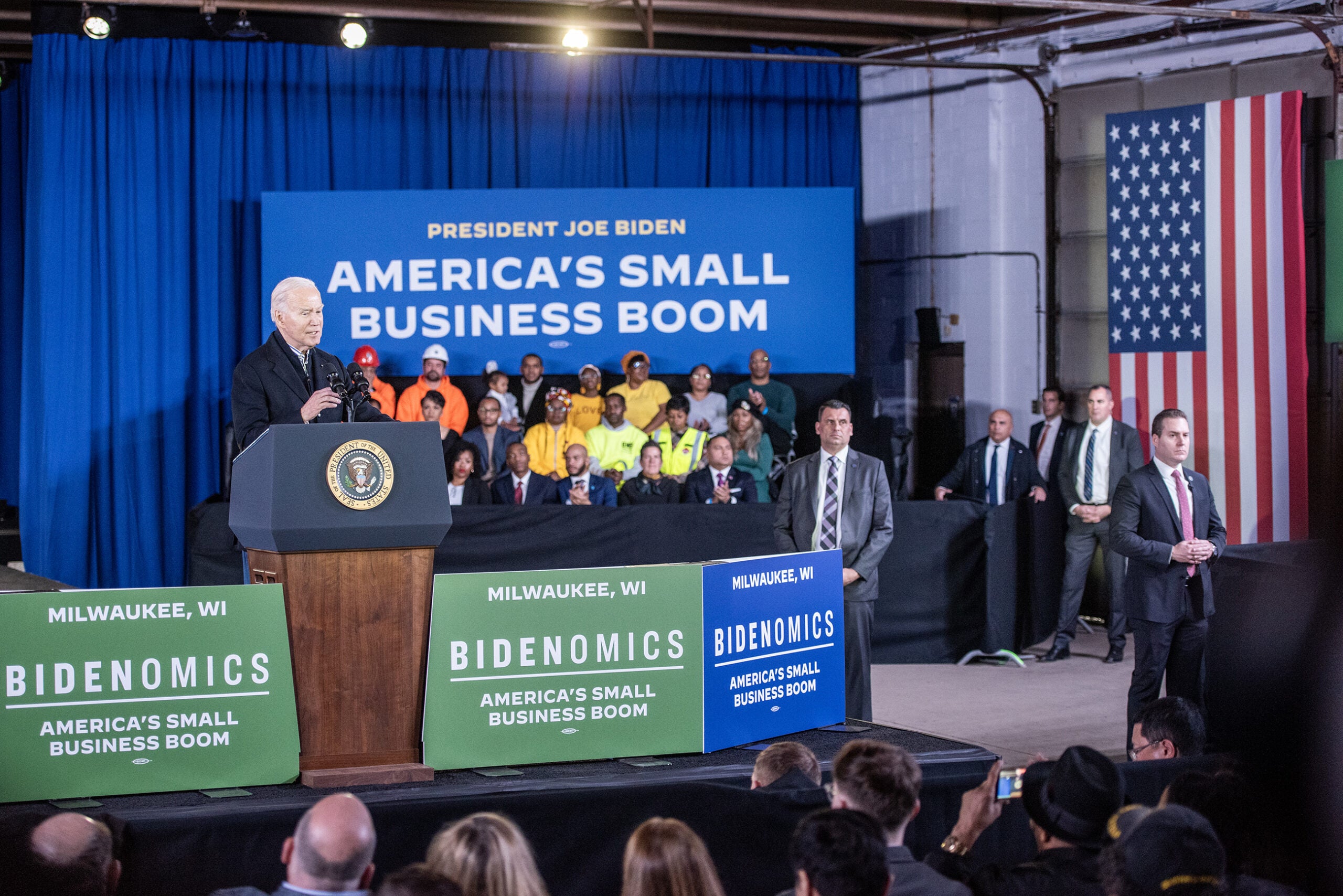 A small crowd listens as Biden speaks from a stage.