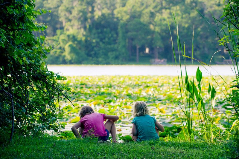 Two girls sit on the shore of a lake