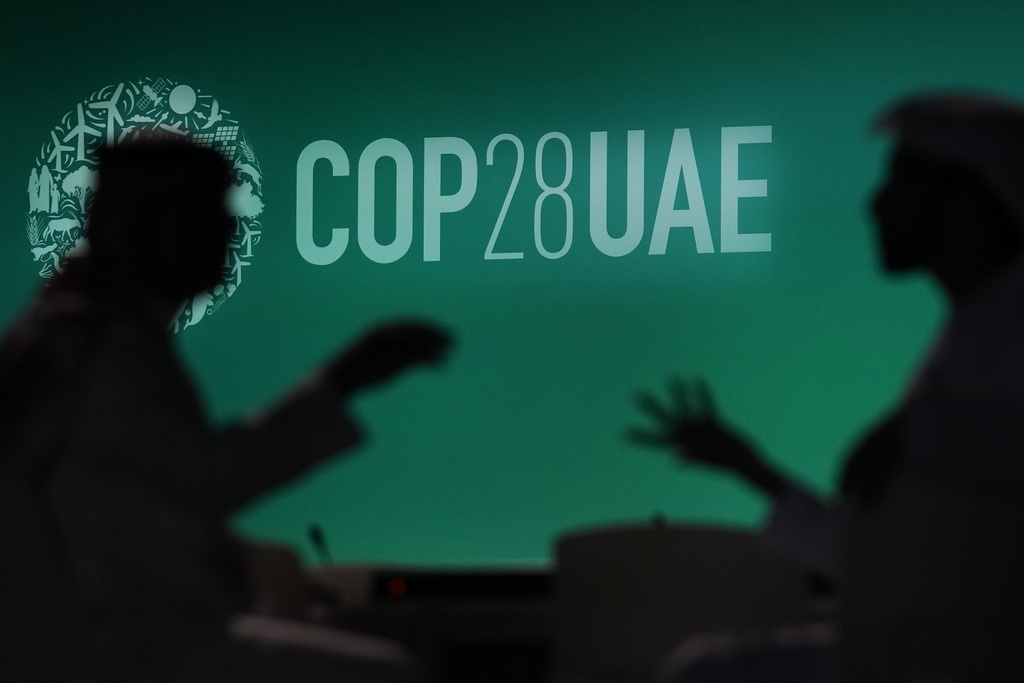 People are silhouetted against a logo for the COP28 U.N. Climate Summit, Nov. 29, 2023, in Dubai, United Arab Emirates. (AP Photo/Rafiq Maqbool, File)