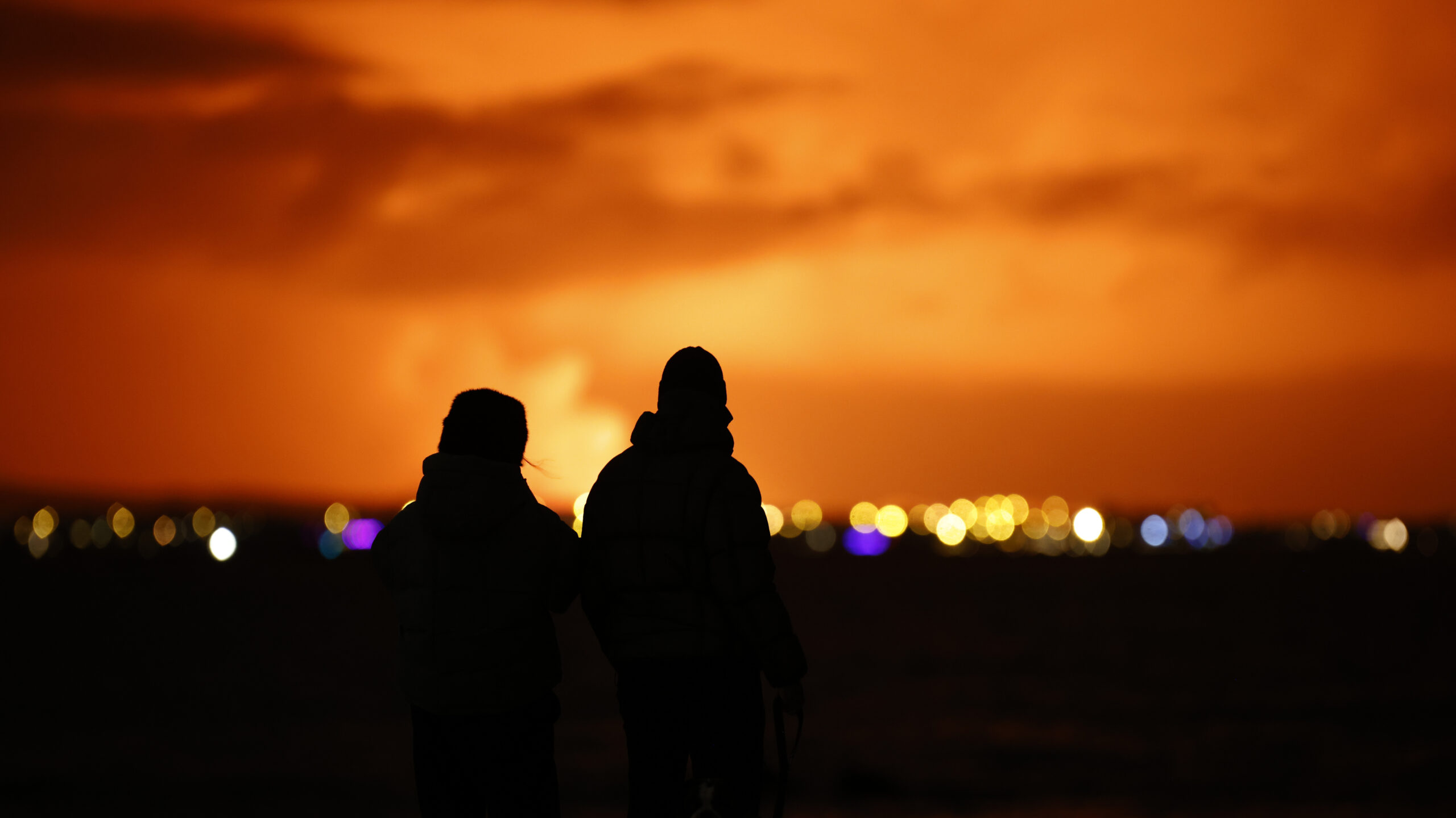 People watch as the night sky is illuminated caused by the eruption of a volcano on the Reykjanes Peninsula in