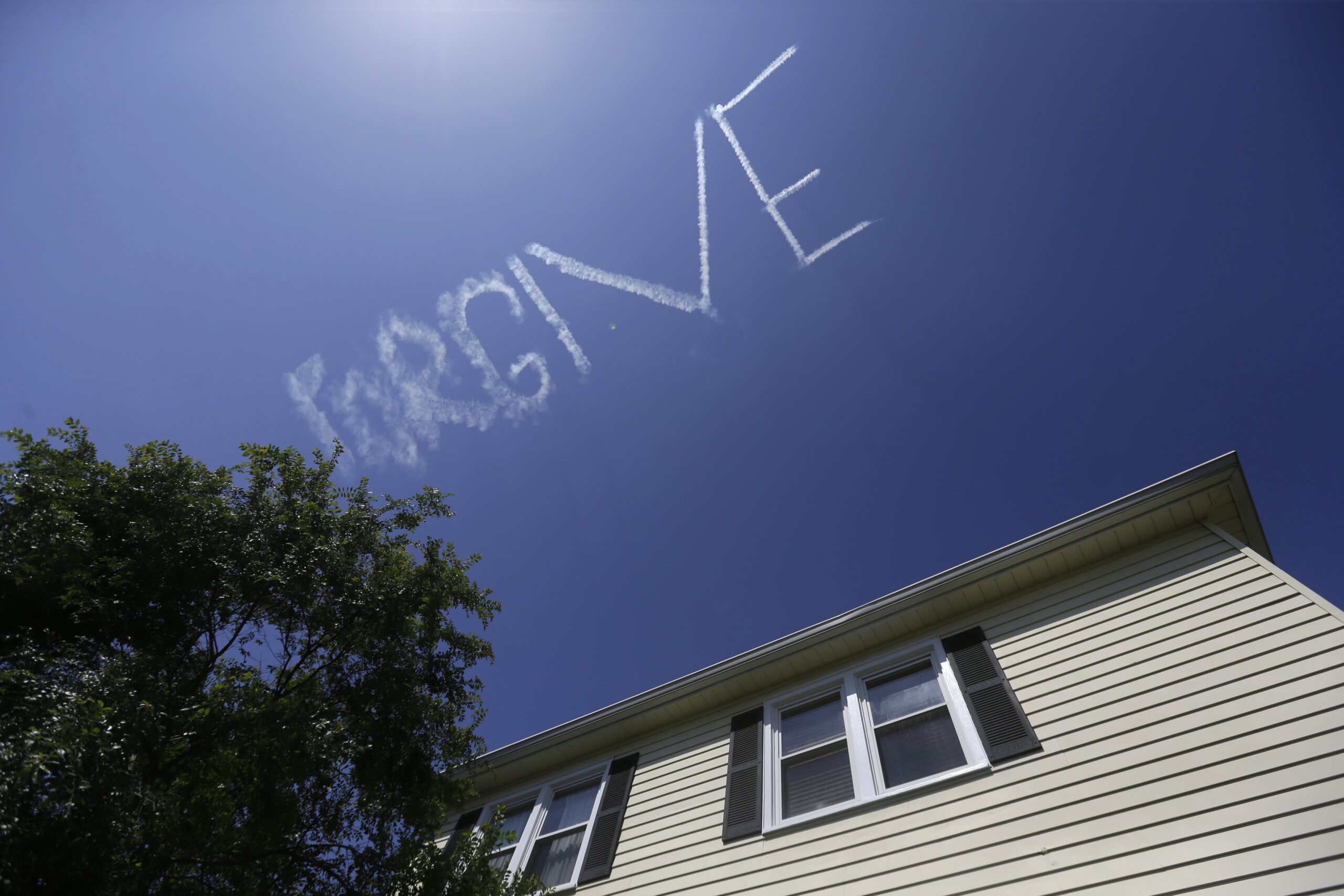 The message "FORGIVE," made by a skywriter, floats above a home in New Orleans.