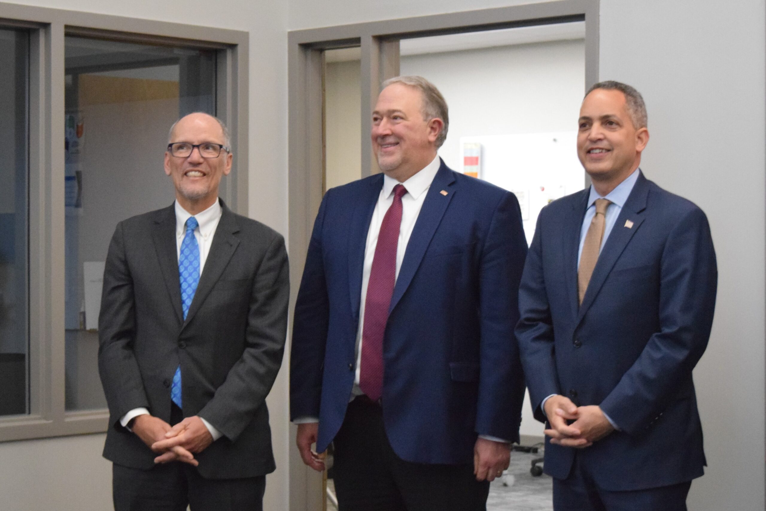 Three men stand in a line smiling during facility tour