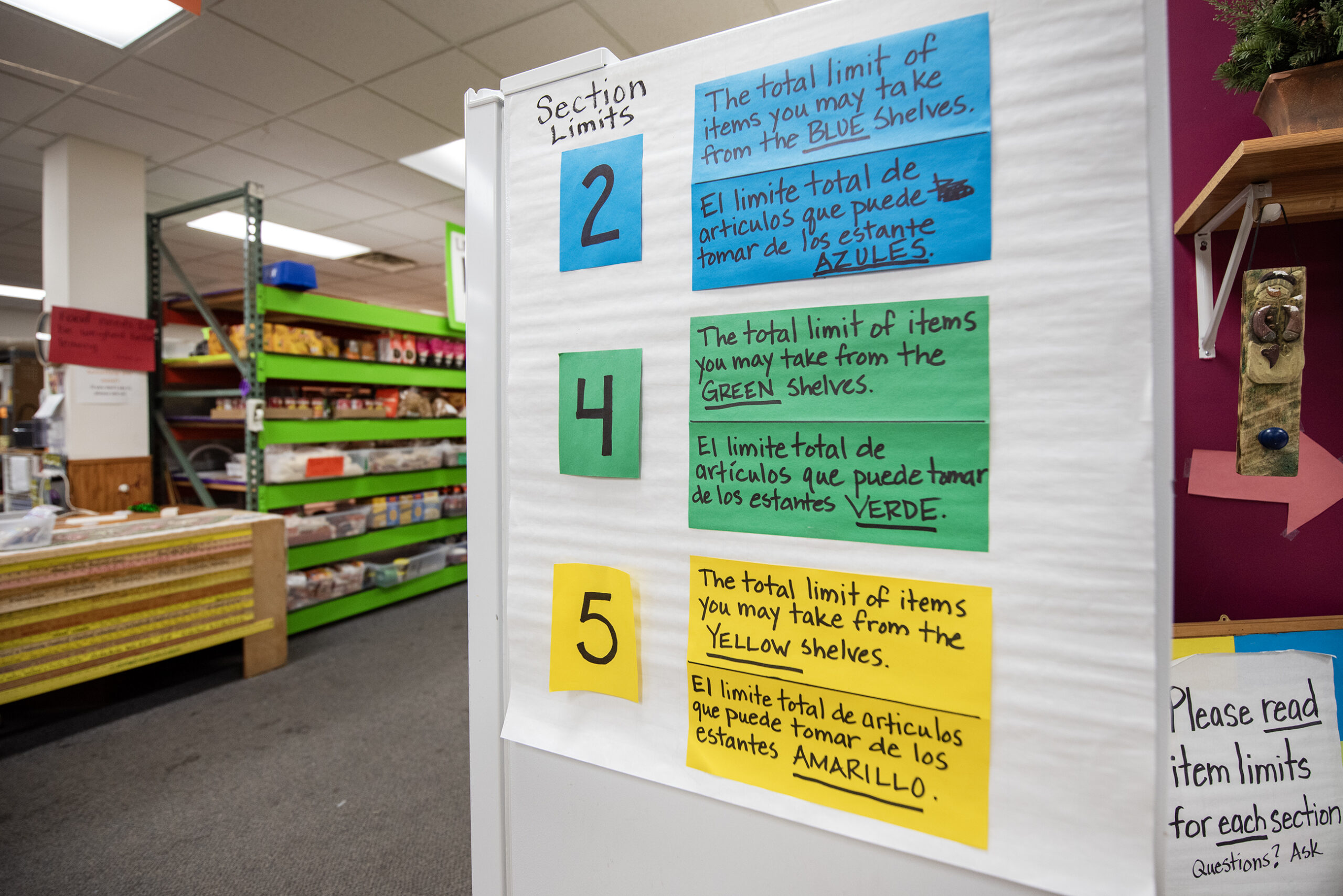 Signs explaining the rules of the food bank are written on colorful strips in English and in Spanish.