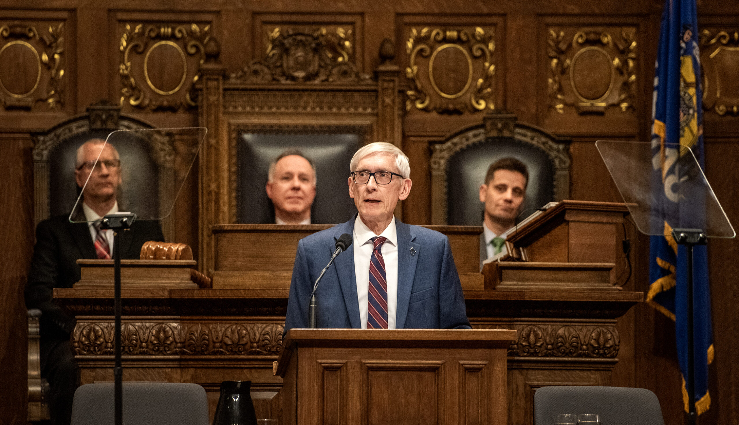 Gov. Evers stands in the Assembly chamber delivering a speech from the podium.