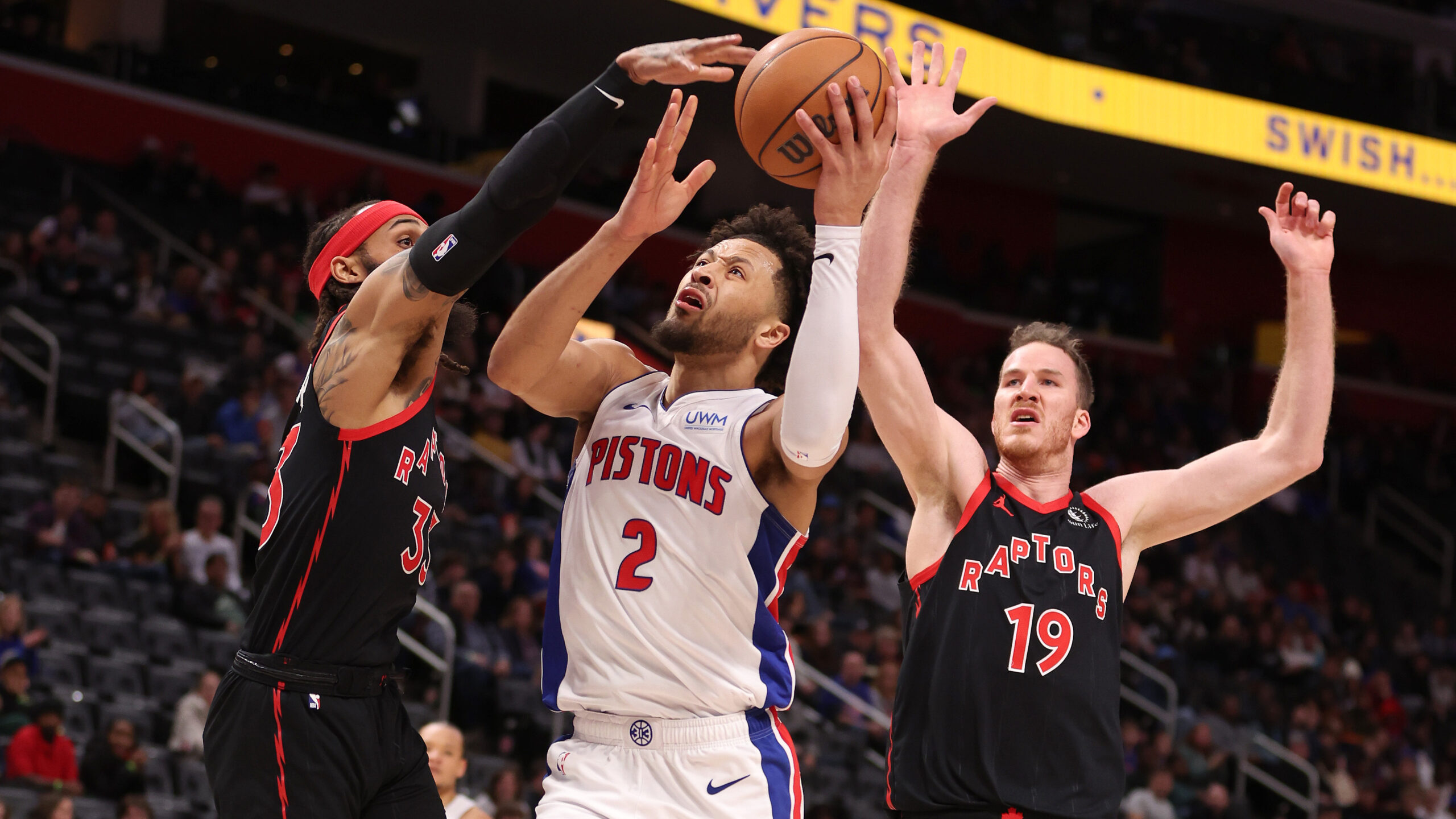 Cade Cunningham #2 of the Detroit Pistons drives to the basket between Gary Trent Jr. #33 and Jakob Poeltl #19 of the