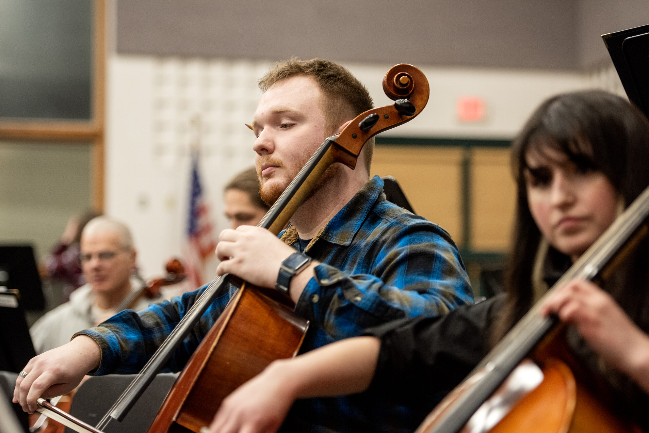 A musician plays the cello while sitting with other musicians in practice.