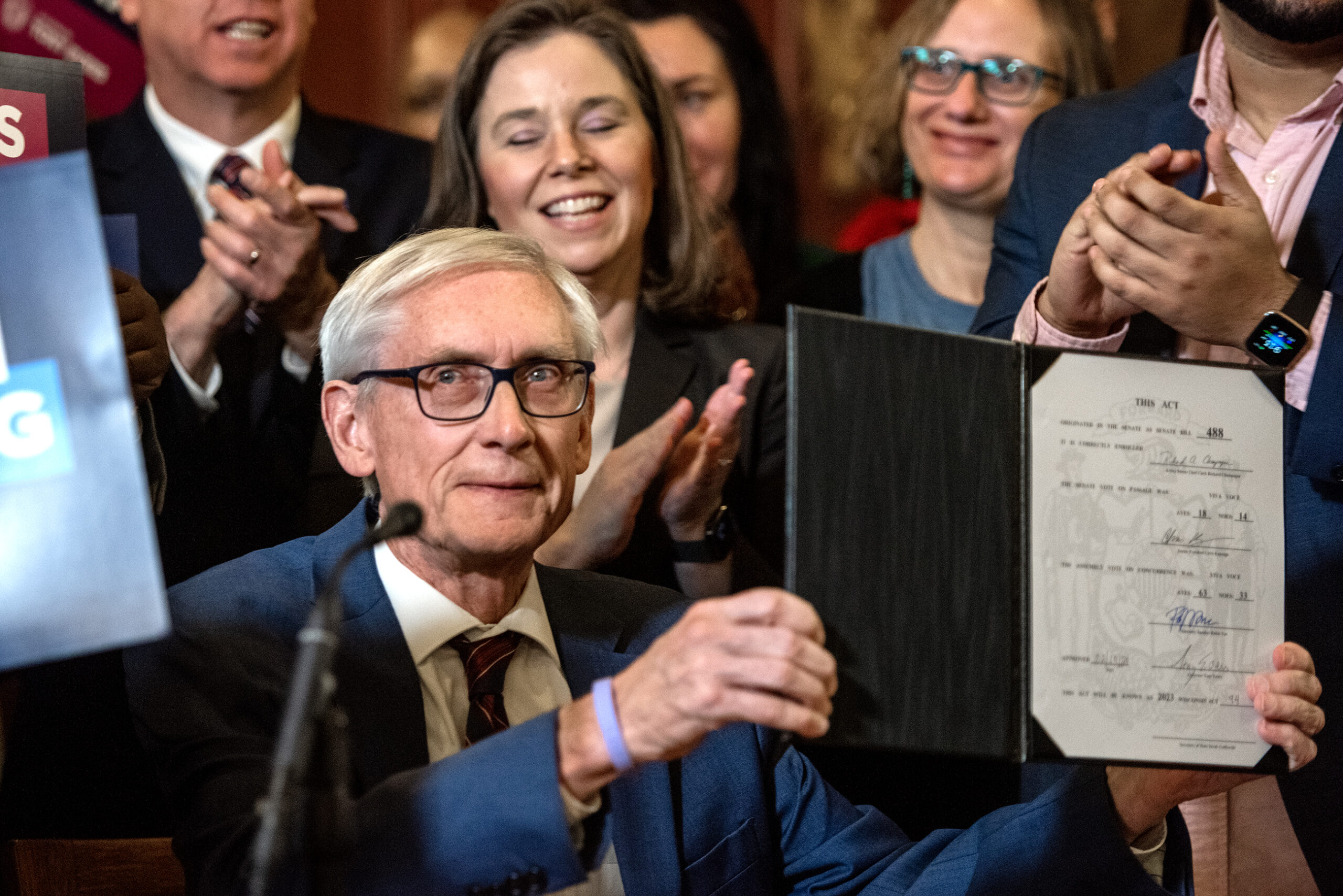 The governor holds up a folder showing the signed bill to the crowd.