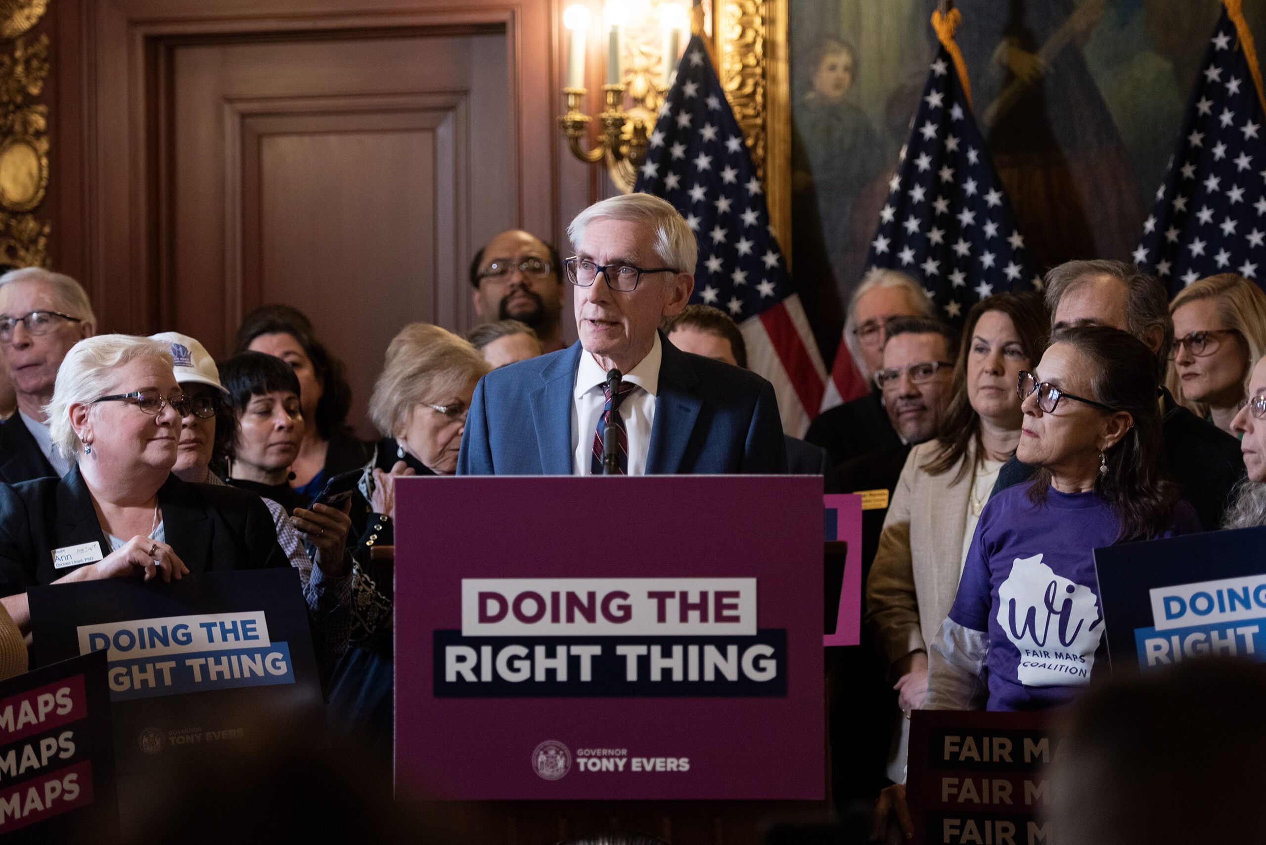 Gov. Evers speaks at a podium behind a sign that says "Doing the right thing." Supporters stand behind him.