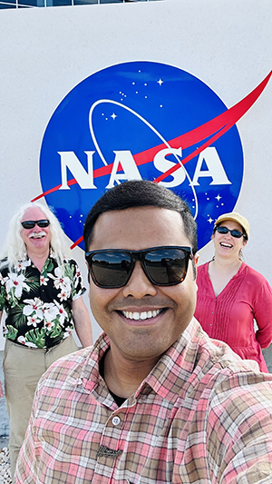 UW-Madison researchers pose and smile in front of a NASA sign.