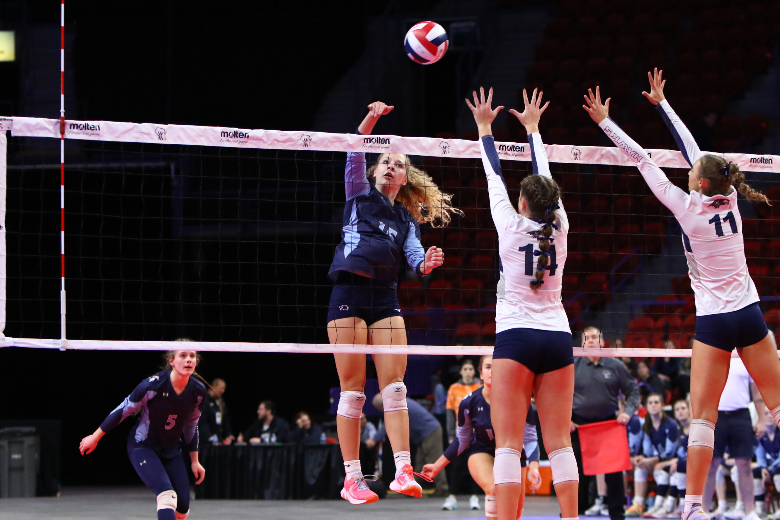A high school girls volleyball athlete attempts to hit the ball away from two opposing players.