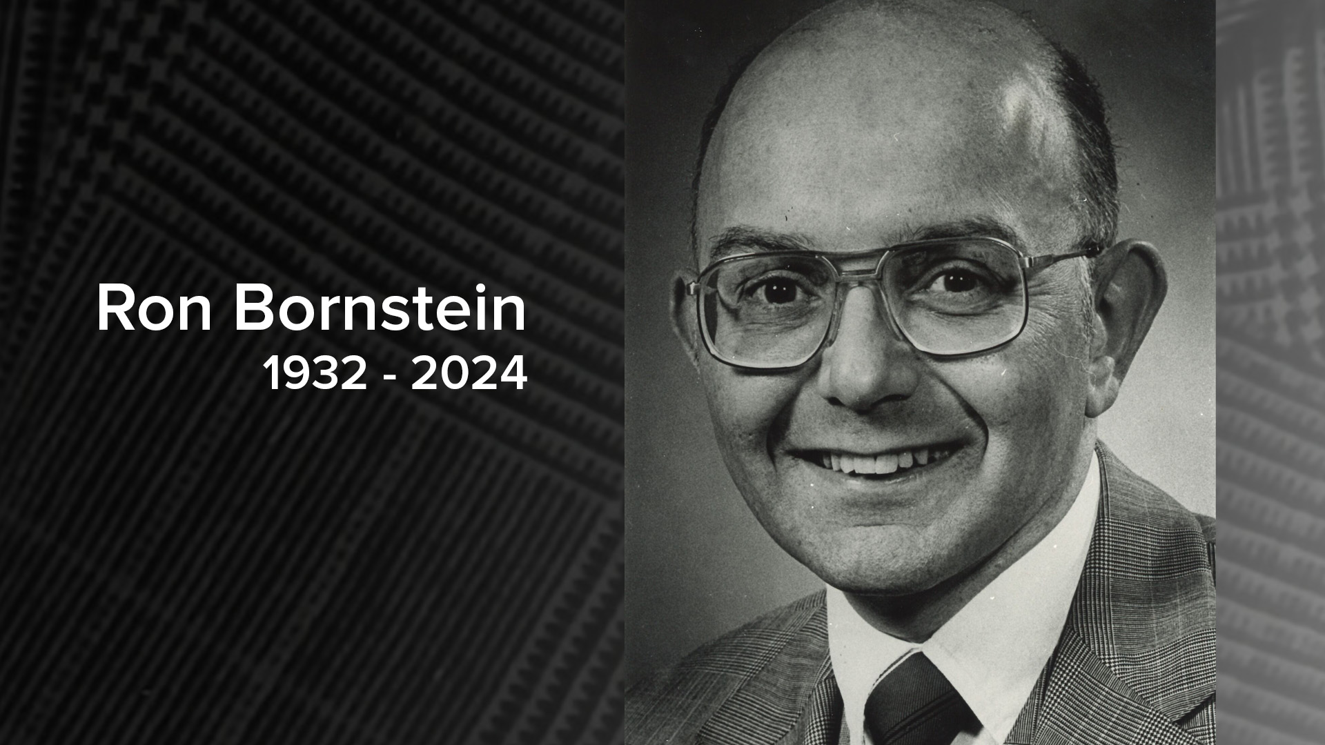 A black and white photo of Ron Bornstein, smiling while wearing glasses and a suit approximately in the 1980s.