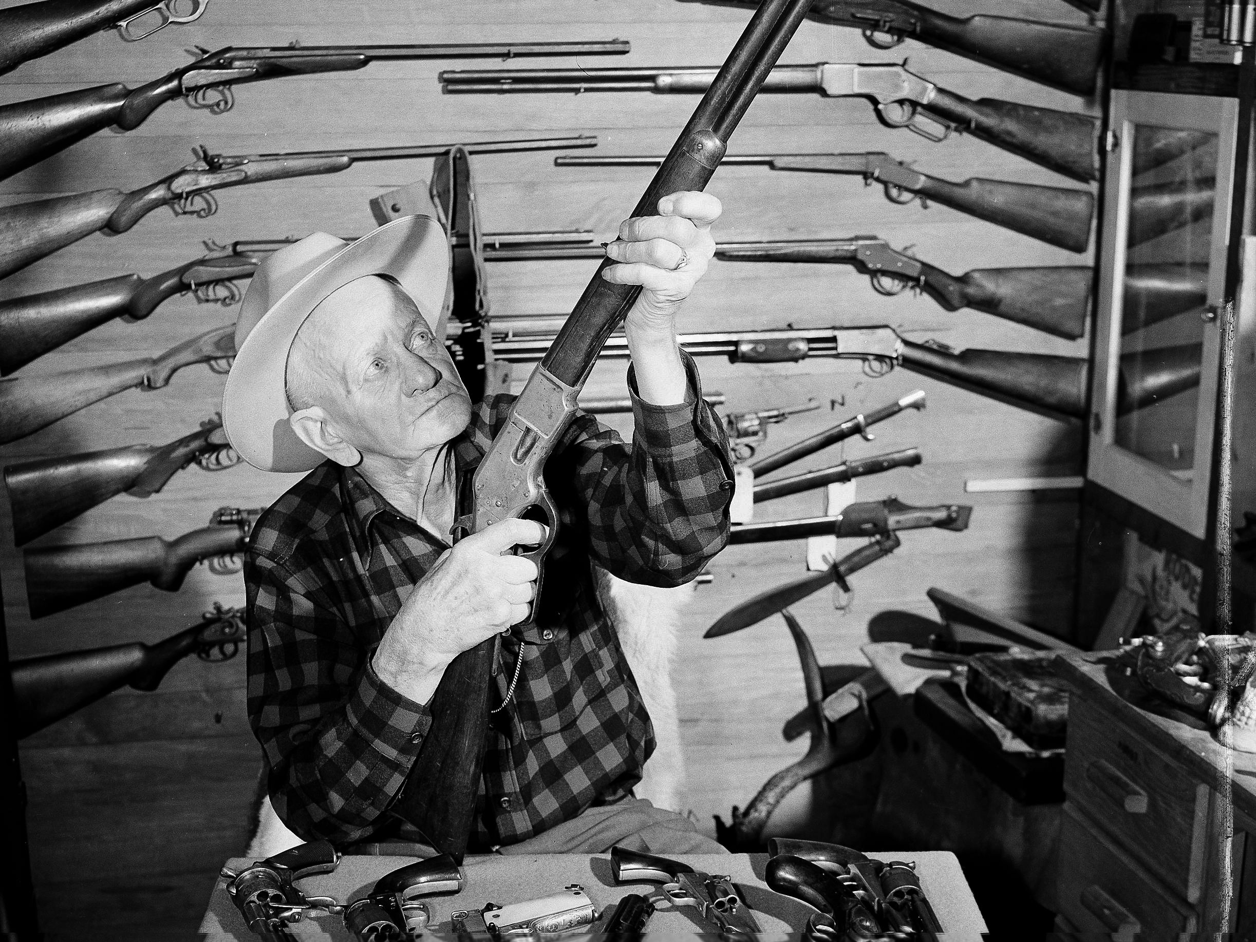 C.J. Hurst of West Covina, Calif., holds up a .44-caliber rimfire Model 66 Winchester rifle as he poses with his collection of about 600 antique guns in 1952.