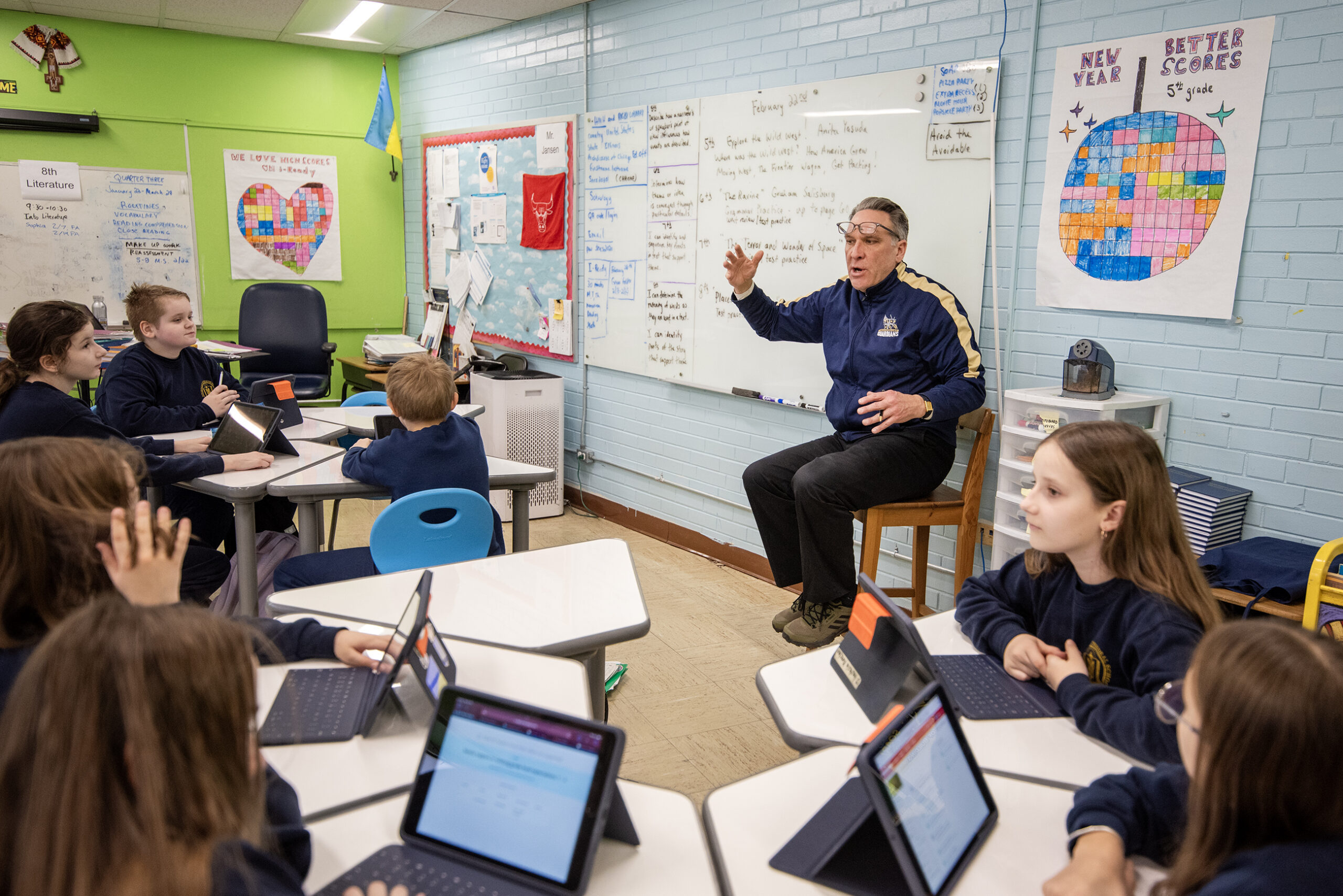 A teacher sits in front of class and gestures to students.