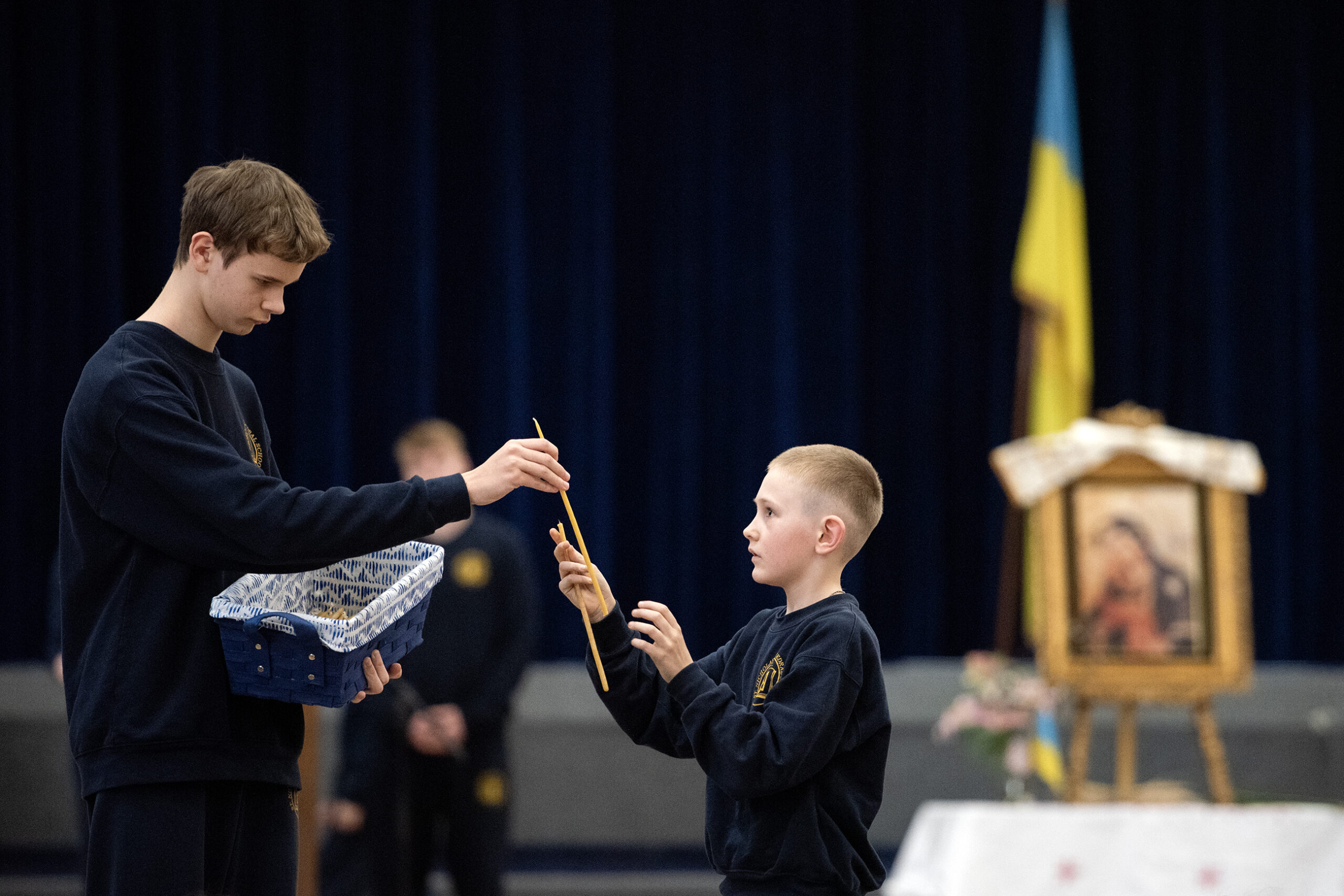 A boy hands another boy a candle.